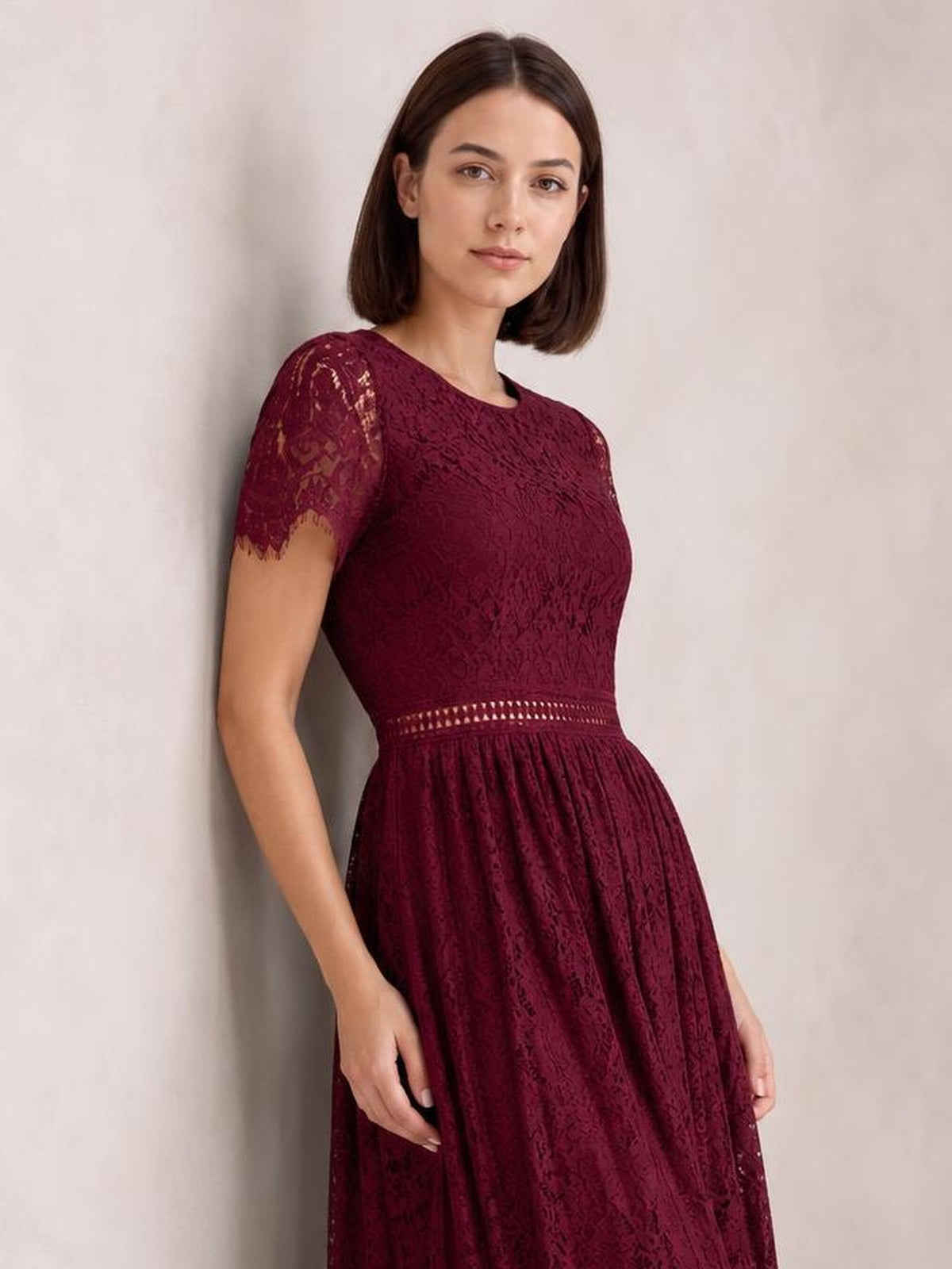 Model poses in a burgundy lace maxi dress with short scalloped sleeves, a fitted bodice, defined waist, and softly gathered A-line skirt.