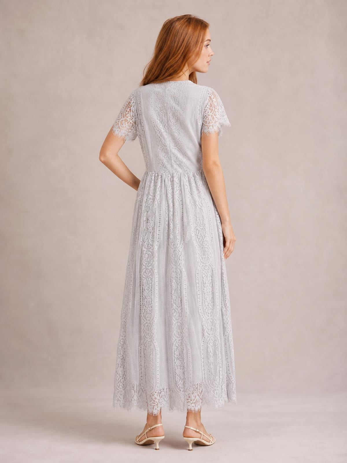 Model shown from behind in a white lace maxi dress with scalloped short sleeves and hem, a fitted waist, and a flowing floor-length silhouette.