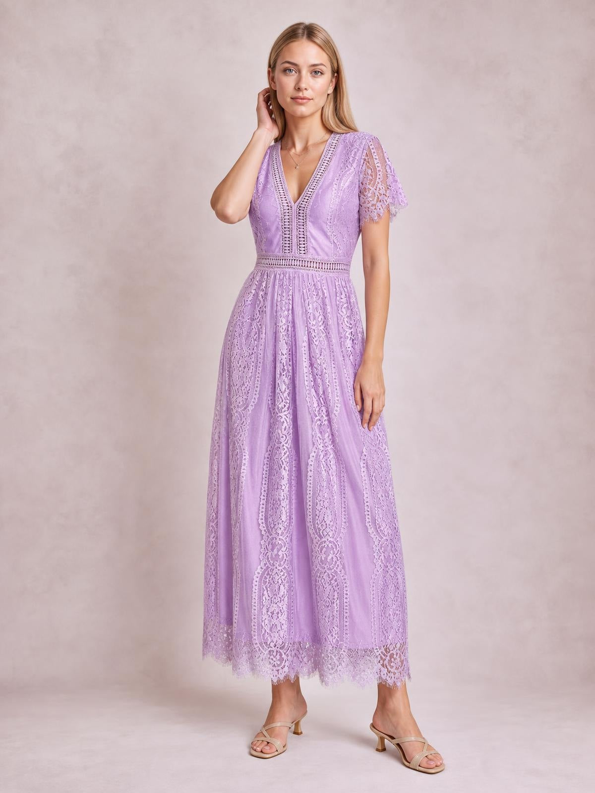 A model poses in a lavender lace plunge maxi dress with a V-neck, short sleeves, fitted waist, flowing silhouette, and scalloped hem.