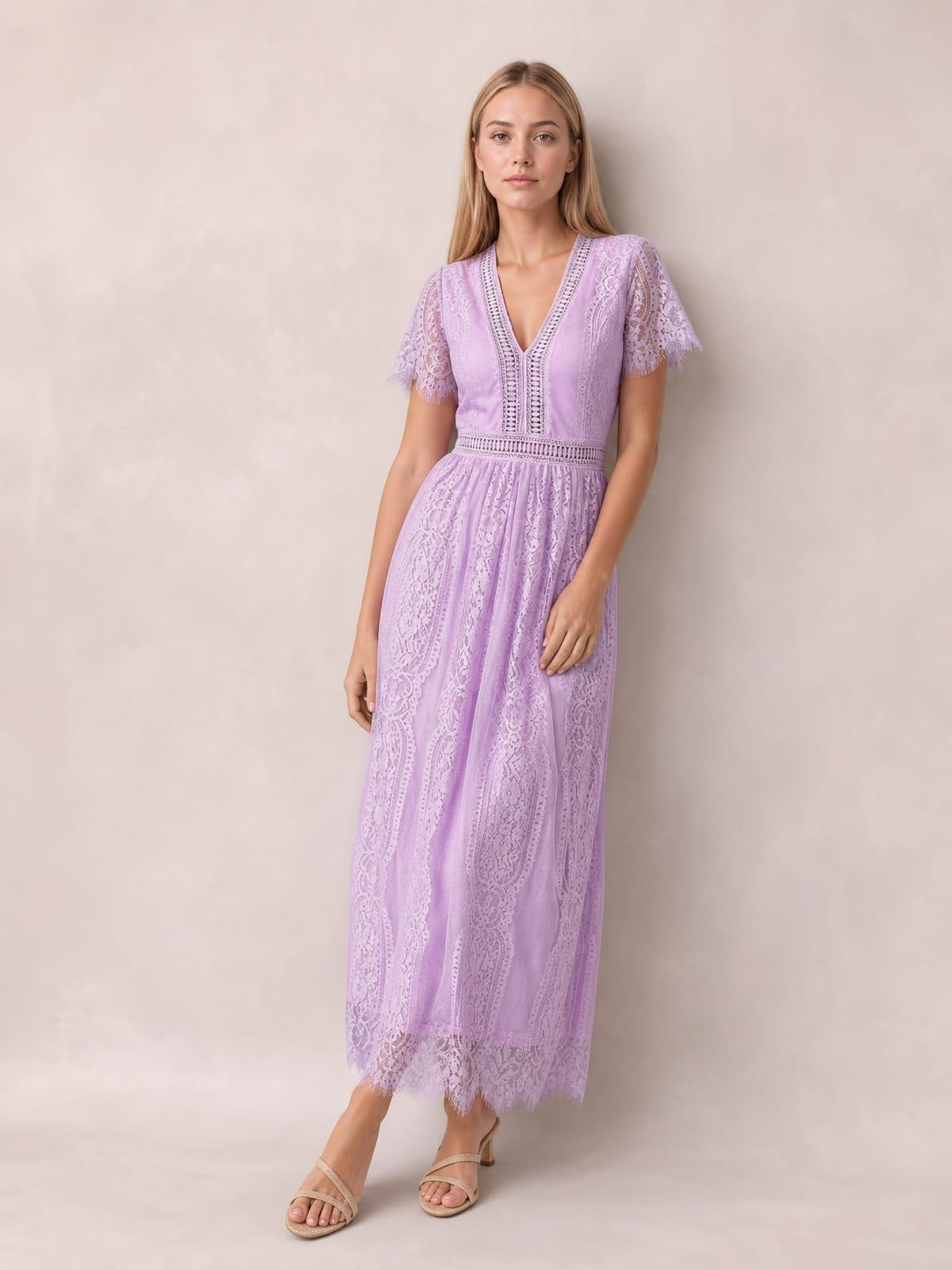 Model wearing a lavender lace maxi dress with a plunge V-neck, short scalloped sleeves, fitted waist, and flowing full-length skirt.