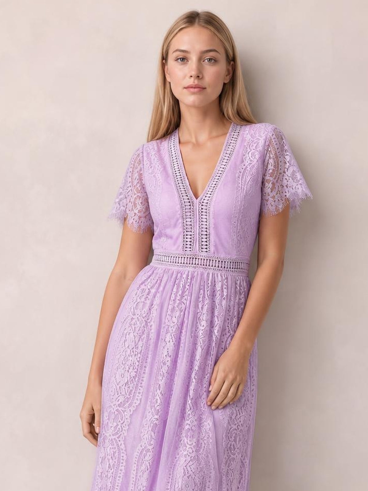 A model wears a lilac lace plunge maxi dress with a V-neck, scalloped short sleeves, defined waist, and flowing pleated skirt.