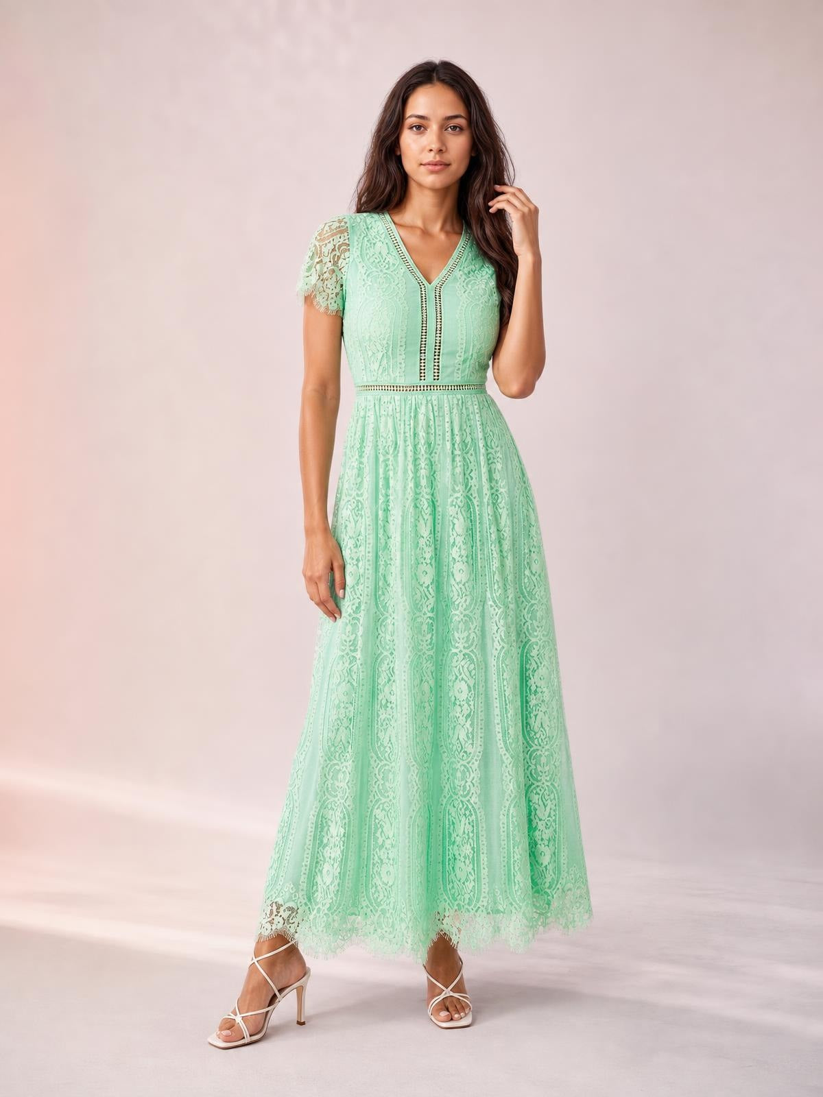 A model poses in a mint green lace plunge maxi dress with a V-neck, short sleeves, fitted waist, flowing silhouette, and scalloped trim.