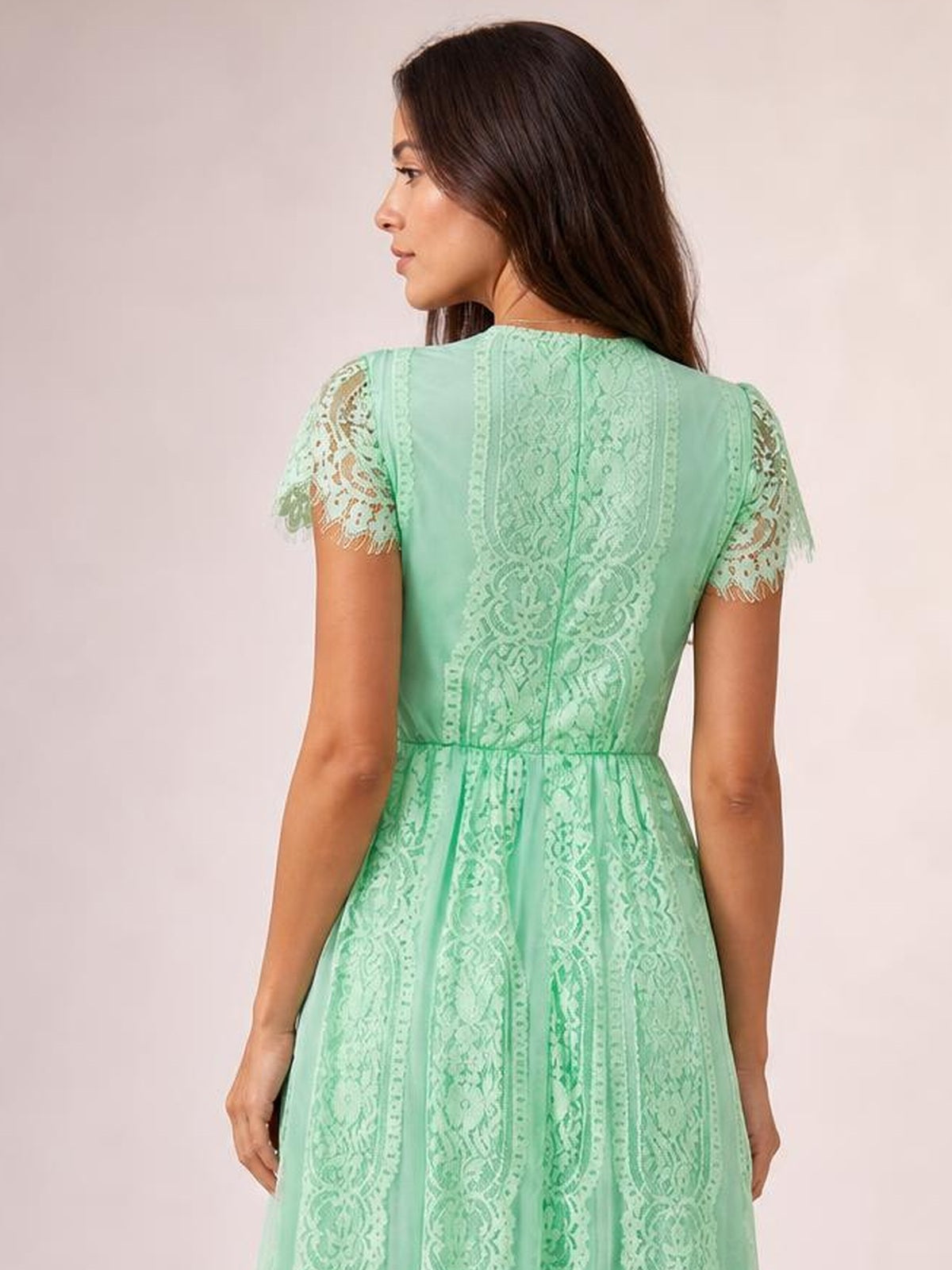 Model faces away wearing a mint green lace maxi dress with scalloped short sleeves, a defined waist, paneled back, and flowing A-line silhouette.