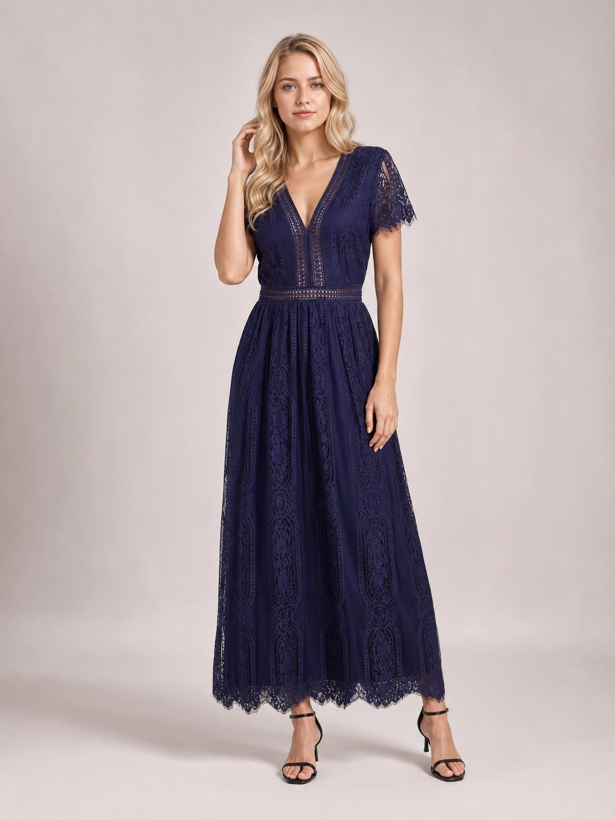 A model poses in a navy lace plunge maxi dress with short sleeves, a fitted waist, flowing A-line skirt, and scalloped trim along the hem.