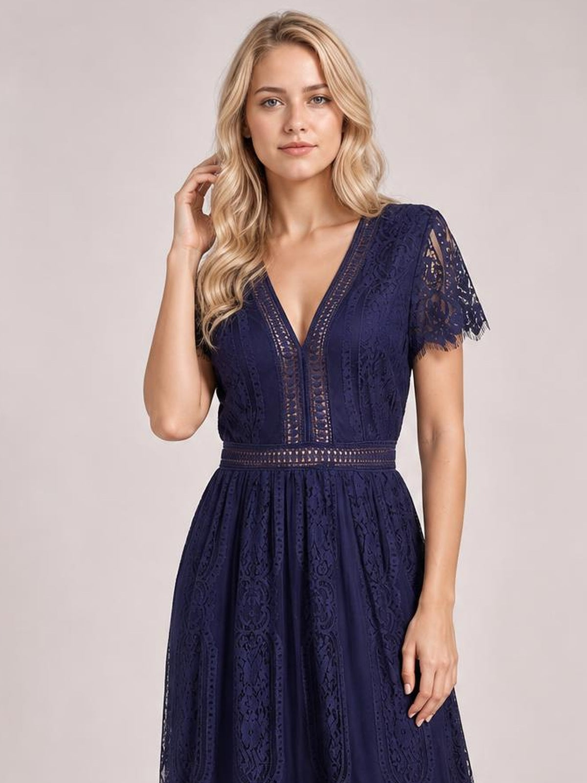 Model poses in a navy scalloped-trim lace plunge dress with short sleeves, a defined waist, and a flowing maxi-length silhouette.