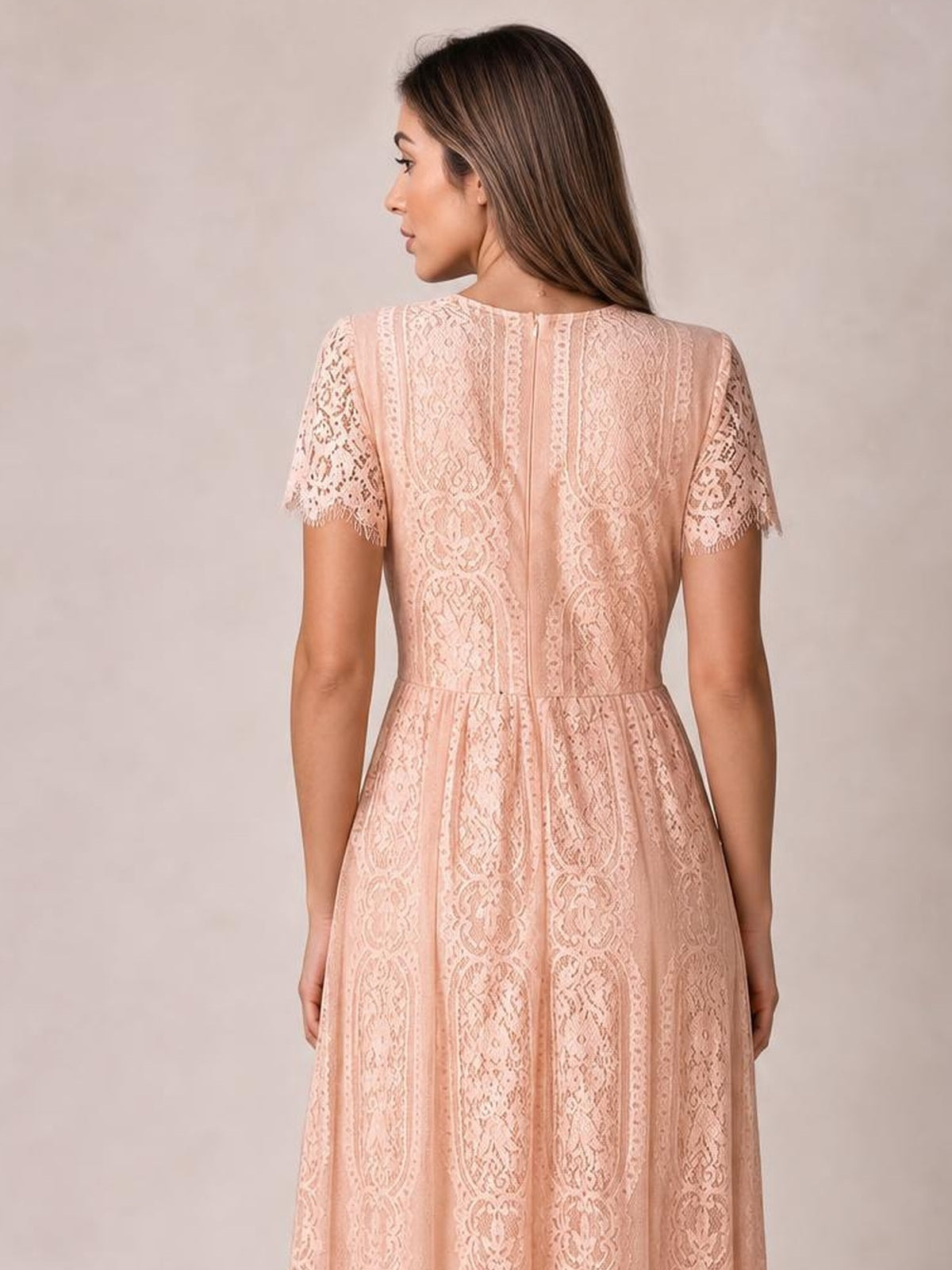 A model stands wearing a blush pink scalloped-trim lace maxi dress with short sleeves, a fitted waist, and a softly flared silhouette.