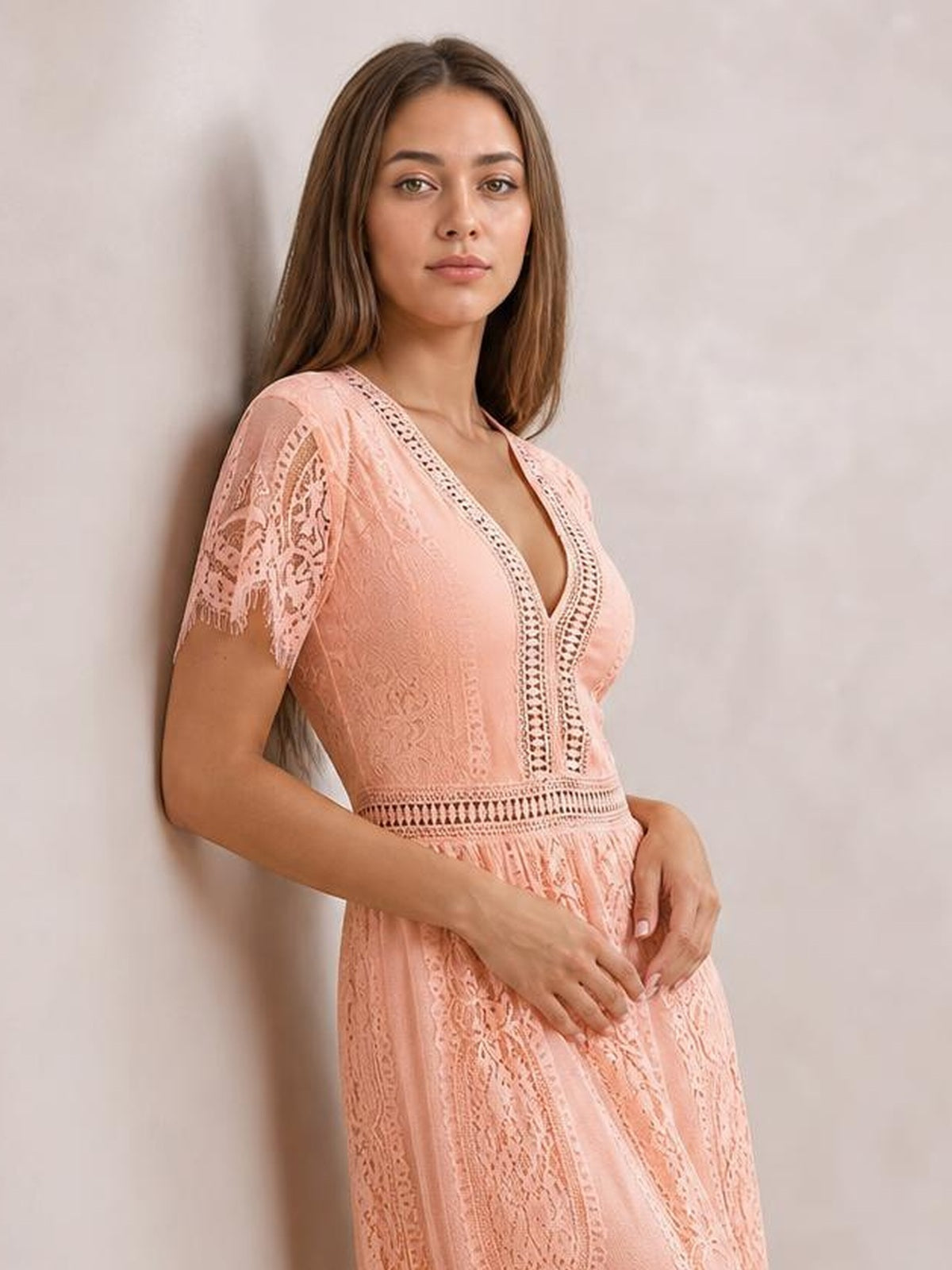 Model poses in a peach maxi dress with a plunging V-neck, scalloped lace trim, short sleeves, fitted waist, and flowing lace skirt.
