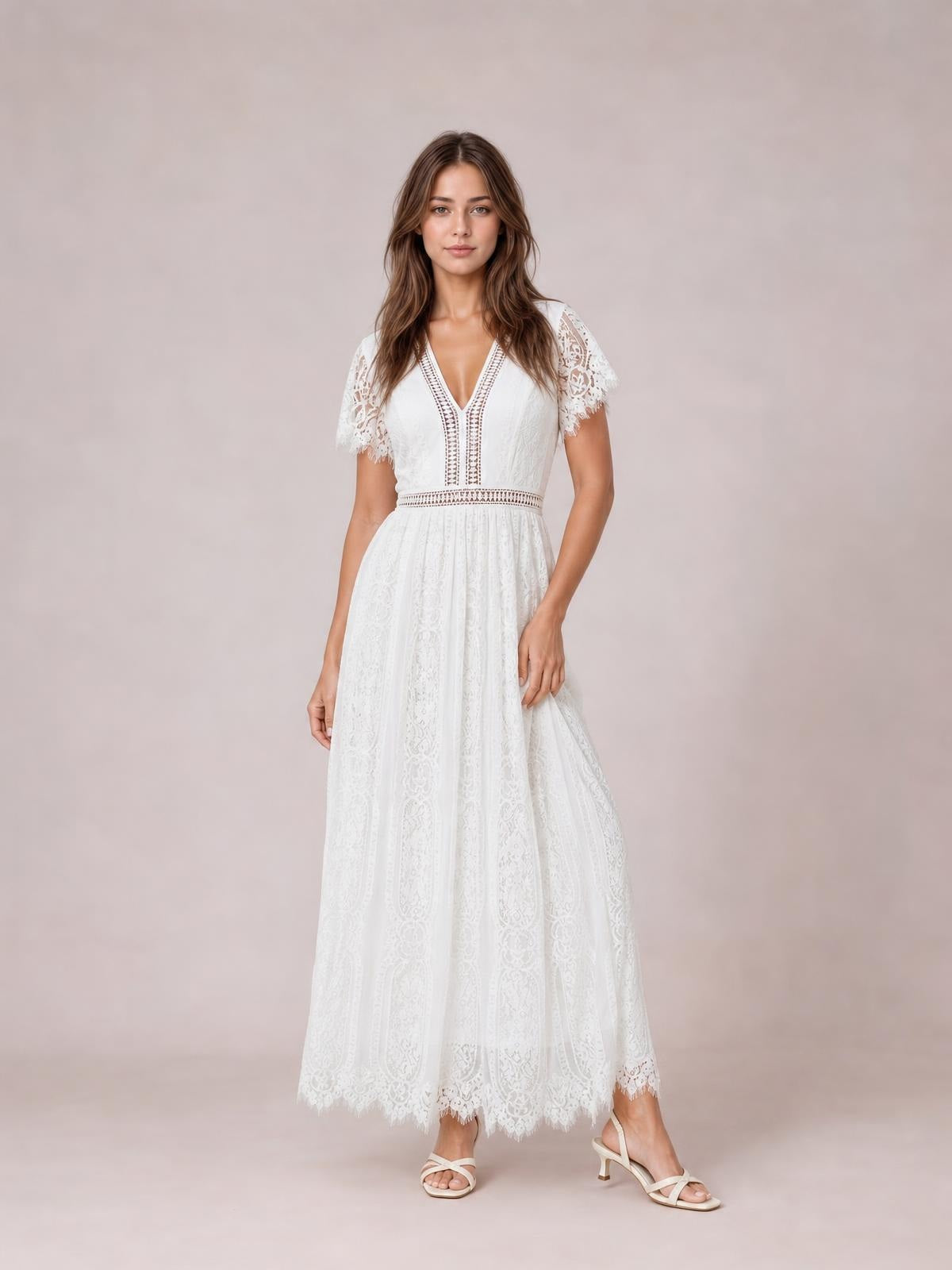 Model stands in a white lace plunge maxi dress with short scalloped sleeves, a defined waist, flowing skirt, and scalloped hem, gently lifting the skirt.
