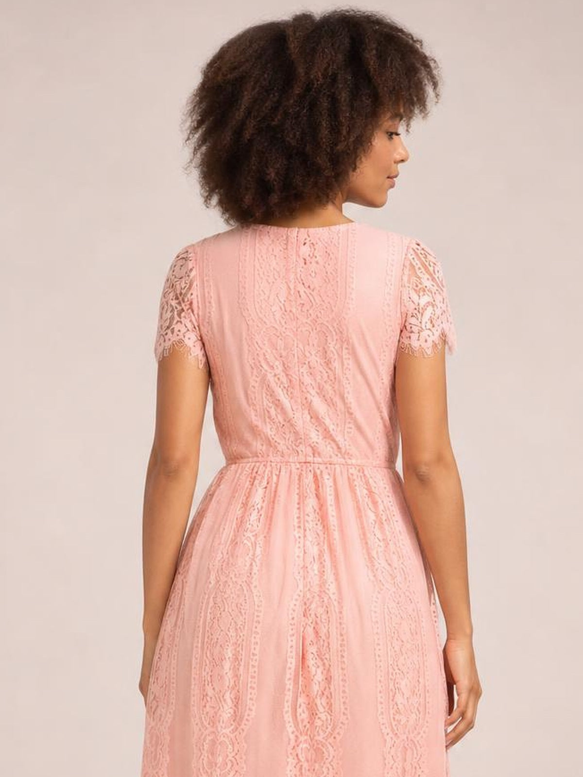 Model shown from the back in a pink lace maxi dress with scalloped-trim short sleeves, a fitted waist, and a flowing, softly flared silhouette.