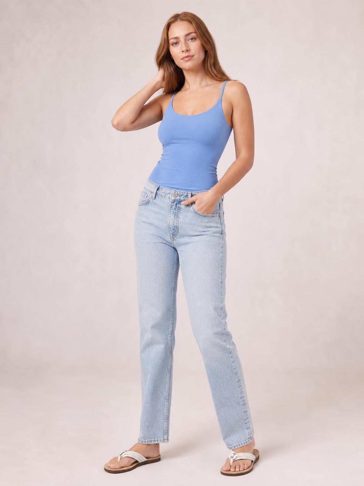 Model poses in a fitted blue scoop neck cami with slim straps and a smooth stretch silhouette, paired with light-wash straight-leg jeans.
