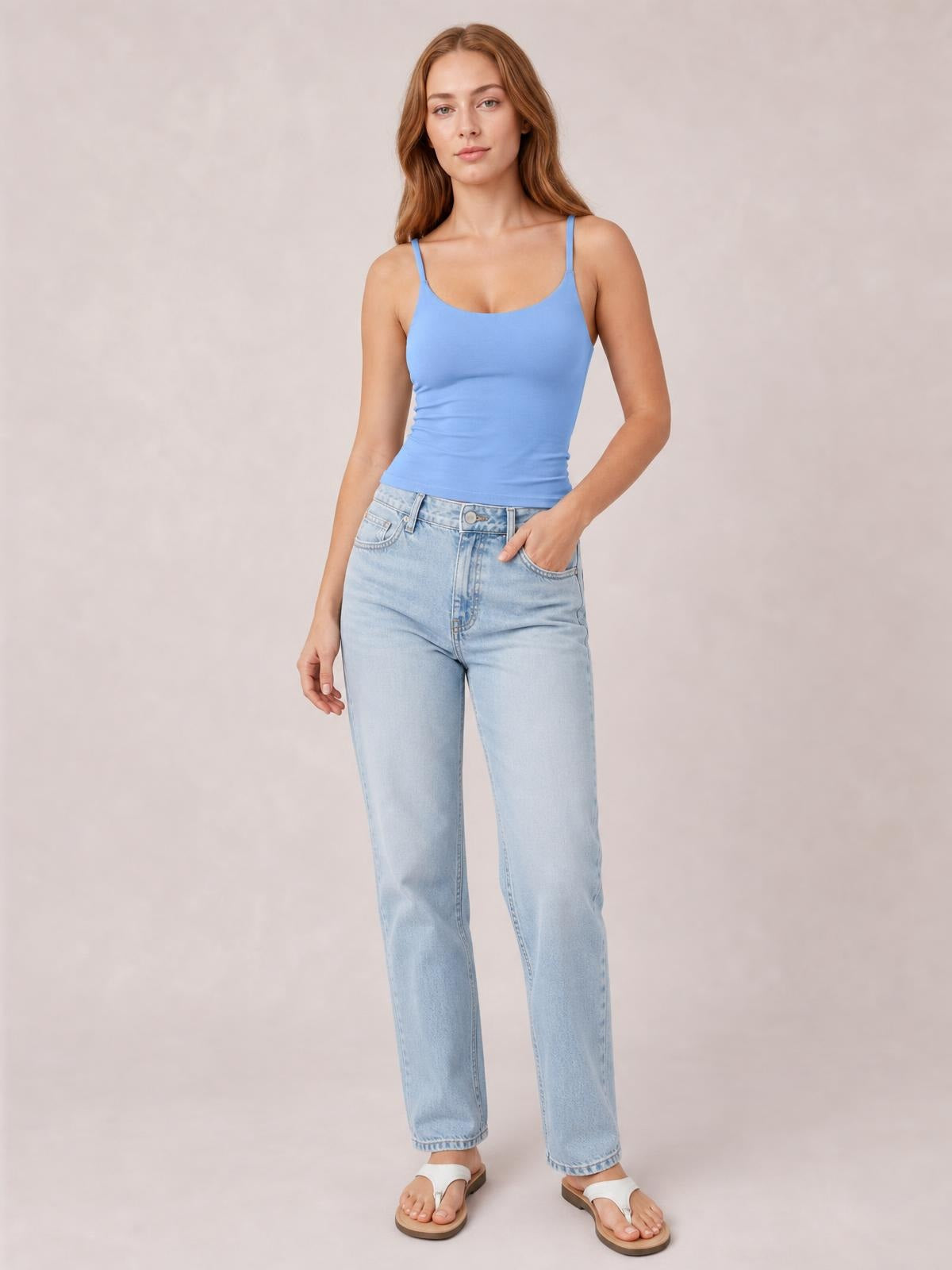 Model in a blue scoop neck cami with thin shoulder straps and a fitted, slightly stretchy silhouette, paired with light-wash jeans.