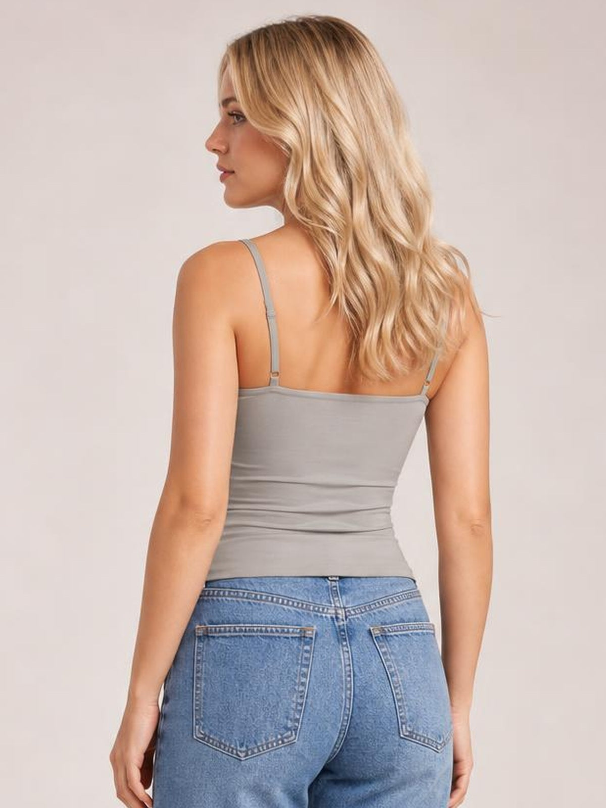 Model turns to show the back of a gray scoop neck cami with thin adjustable straps and a fitted, slightly stretchy silhouette.