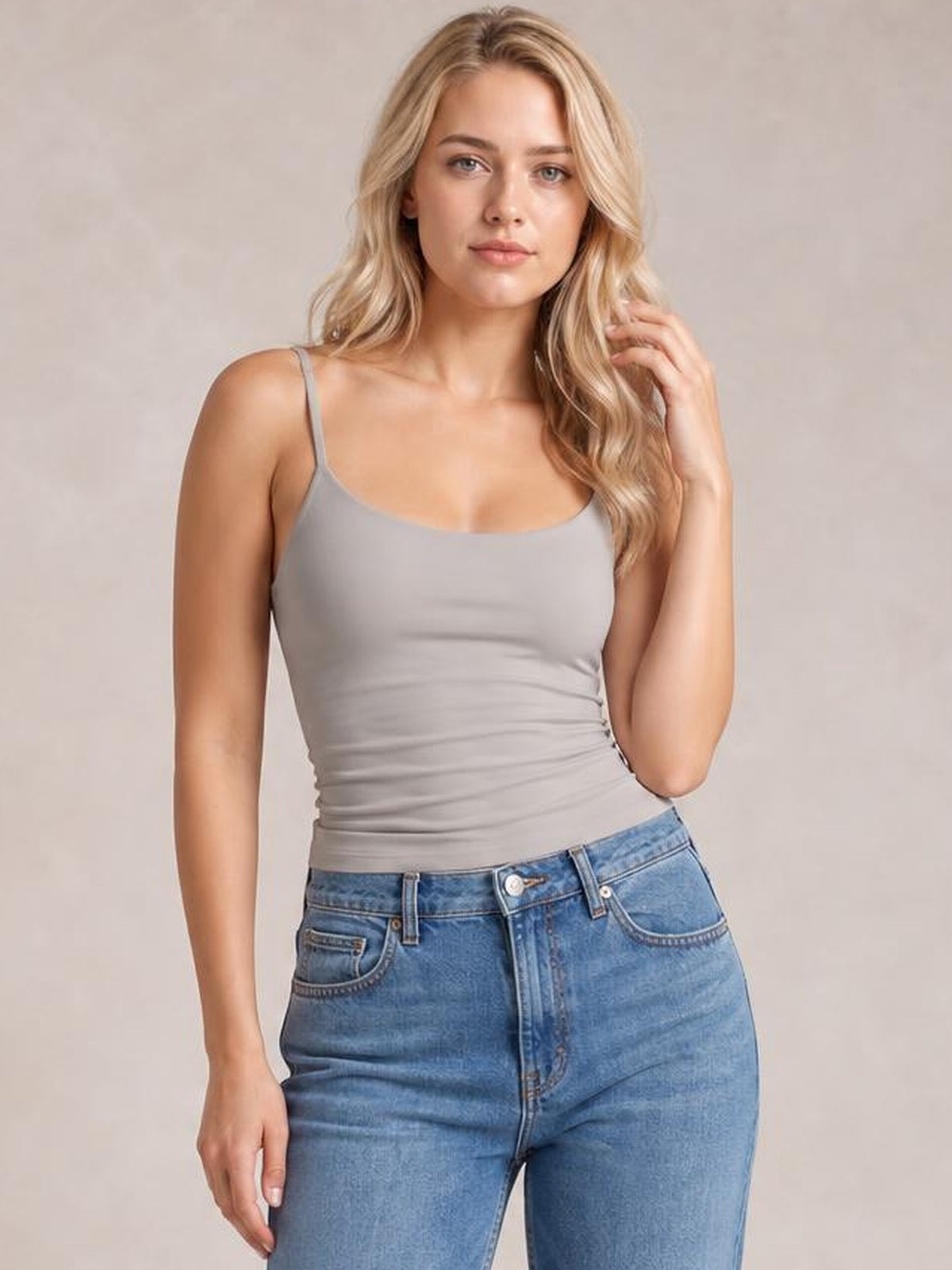 Model in a gray scoop neck cami with thin straps and a fitted, slightly ruched silhouette, posing with one hand touching her hair.