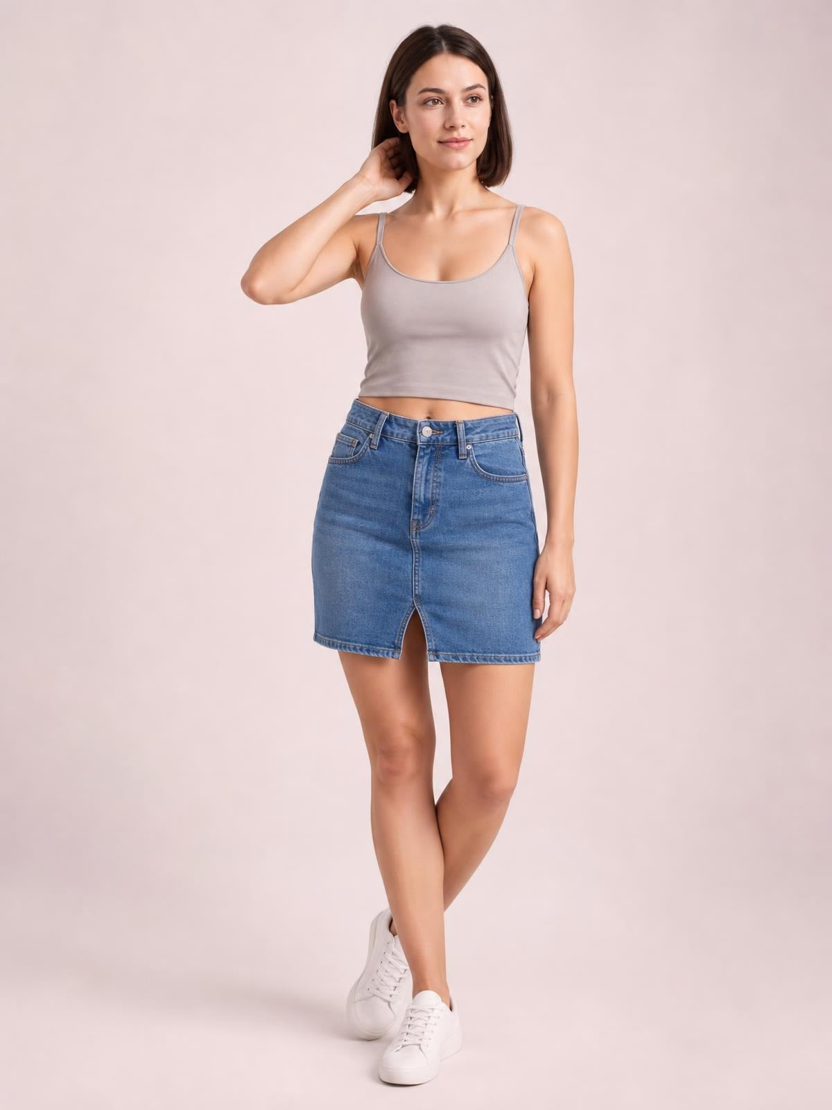 A model wears a taupe scoop-neck cropped cami with slim shoulder straps and a fitted silhouette, posing with one hand near her hair and crossed legs.