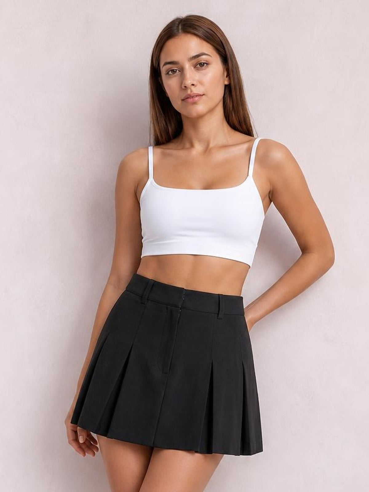 A model wears a white scoop neck cropped cami with thin shoulder straps and a fitted silhouette, posing with one hand in her pocket.