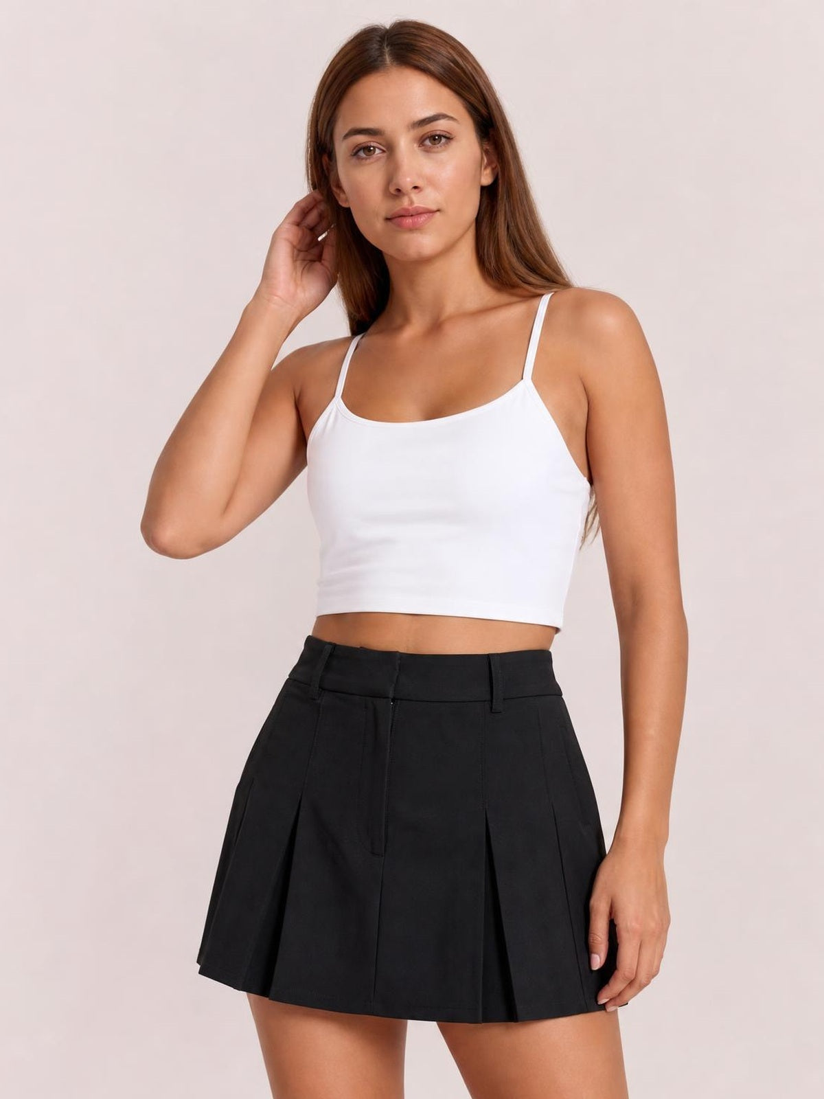 Model poses in a white scoop neck cropped cami with thin straps and a fitted silhouette, featuring visible chest pads and a clean, basic construction.