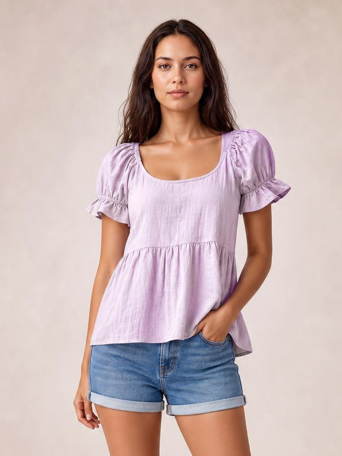 A model stands wearing a solid lavender blouse with a scoop neckline, gathered waist, short puffed flounce sleeves, and a relaxed peplum silhouette.
