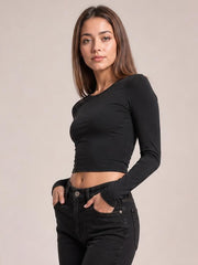 Model poses with hands in her pockets wearing a fitted black scoop neck long sleeve cropped T-shirt with a simple, body-skimming silhouette.