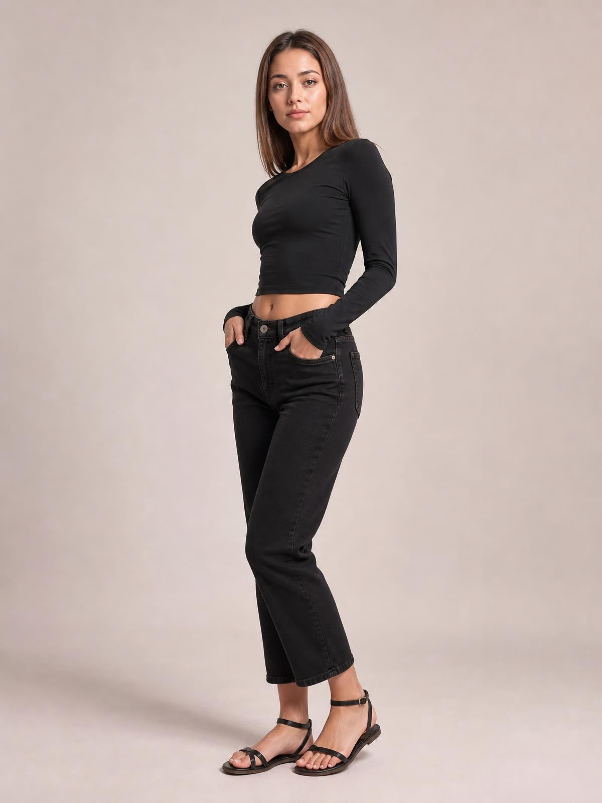 Model poses with hands in pockets wearing a black scoop neck long sleeve cropped T-shirt with a fitted silhouette and slightly stretchy construction.