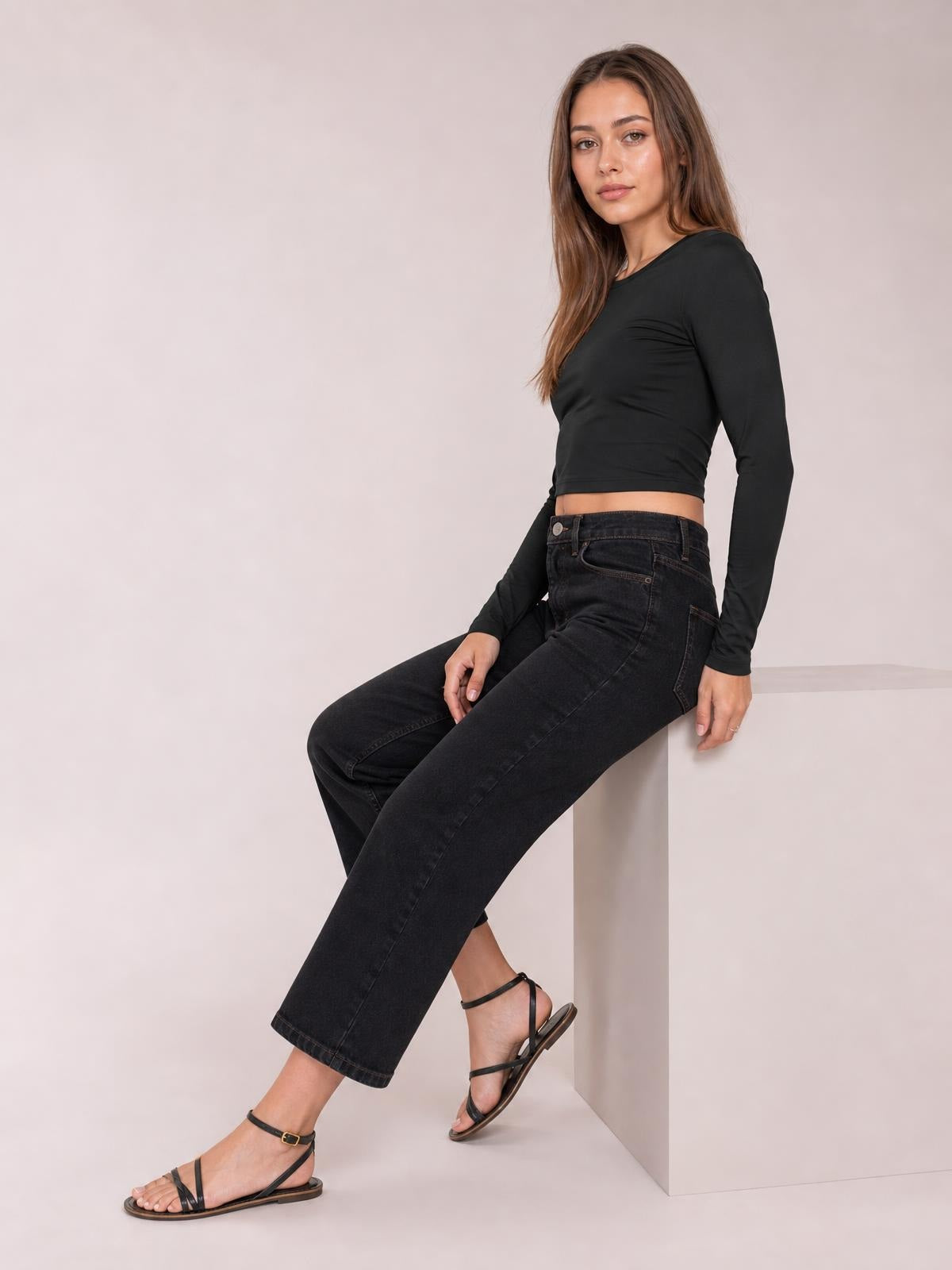 Model seated in a relaxed pose wearing a black scoop neck long sleeve cropped T-shirt with a fitted silhouette and slightly stretchy construction.