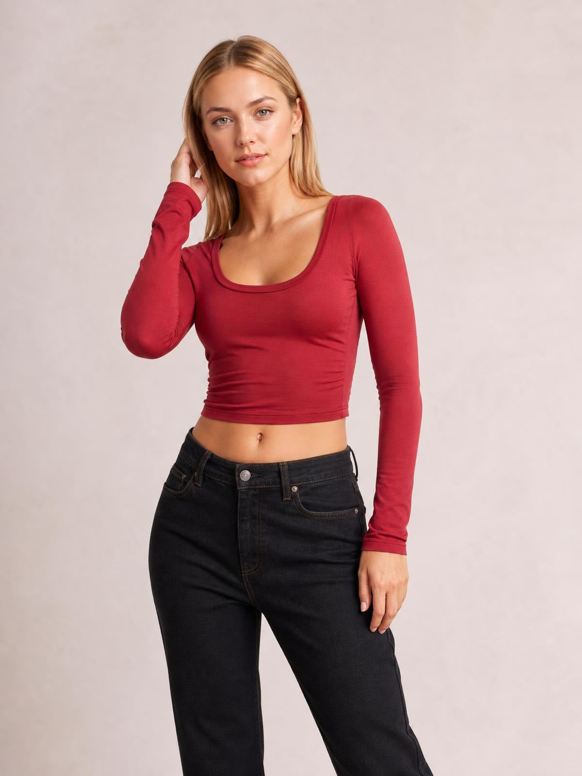 Model poses with one hand near her hair, wearing a fitted red scoop neck long sleeve cropped T-shirt with a smooth, stretch silhouette and finished hem.