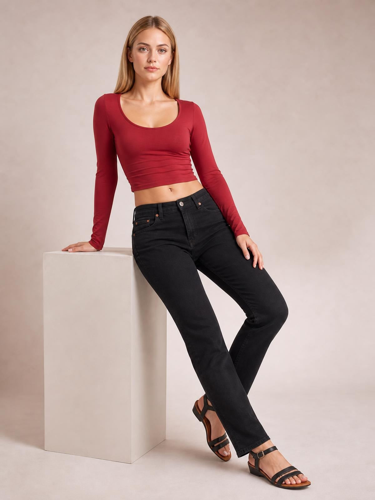 A model leans against a pedestal wearing a fitted burgundy scoop neck long sleeve cropped T-shirt with a smooth, slightly stretchy silhouette.