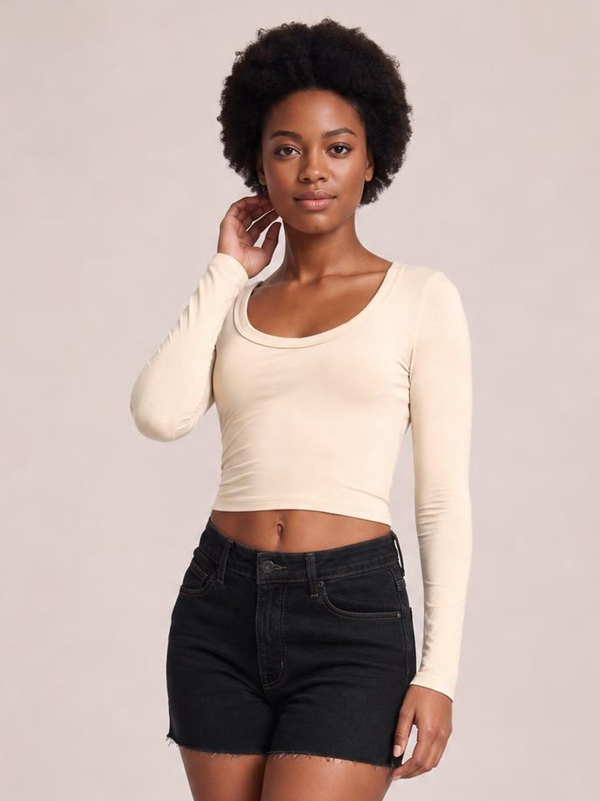 A model poses with one hand near her neck, wearing a cream scoop neck long sleeve cropped T-shirt with a fitted silhouette and clean hem.