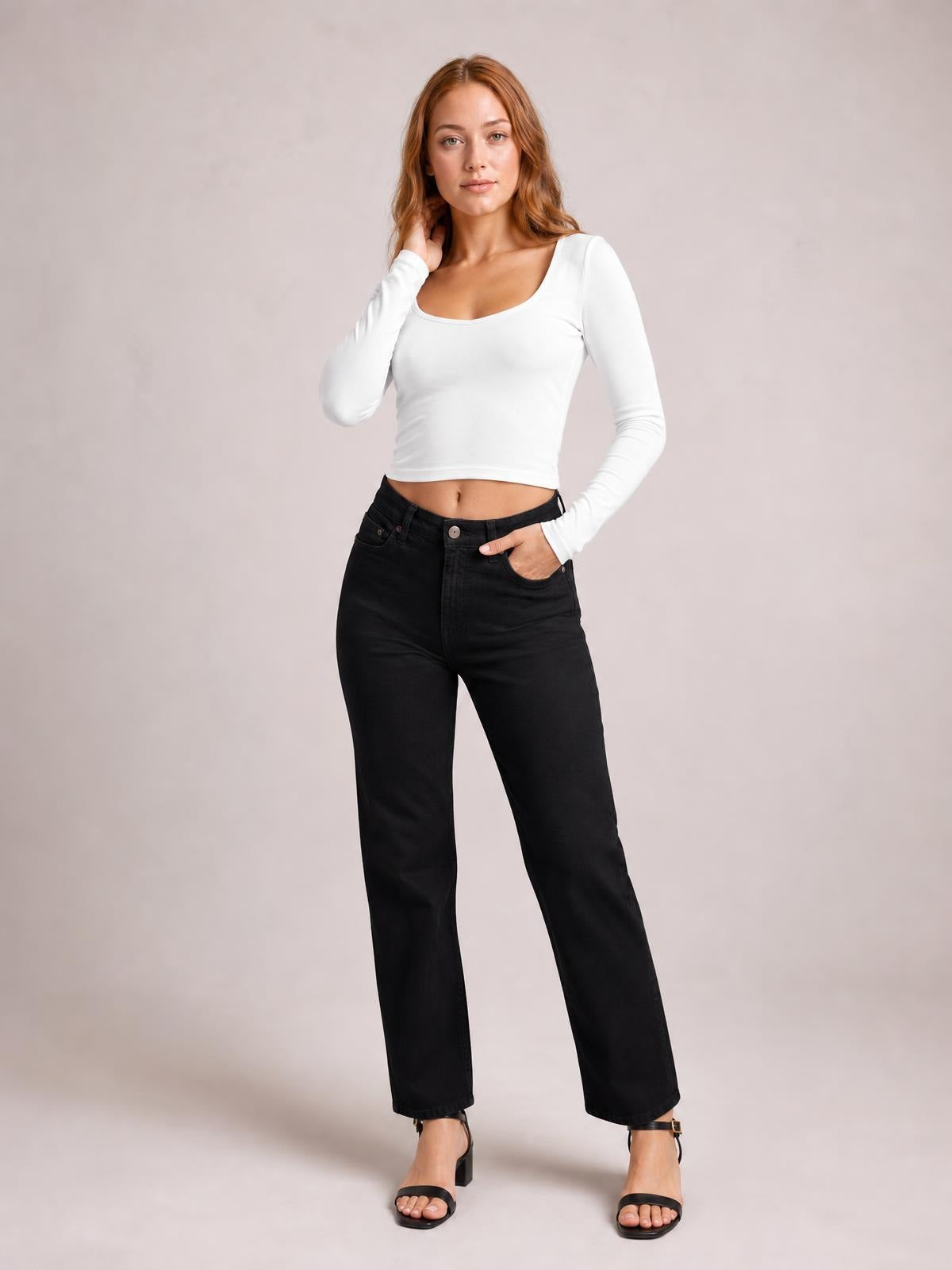 Model poses in a white scoop neck long sleeve cropped T-shirt with a fitted silhouette and exposed midriff.