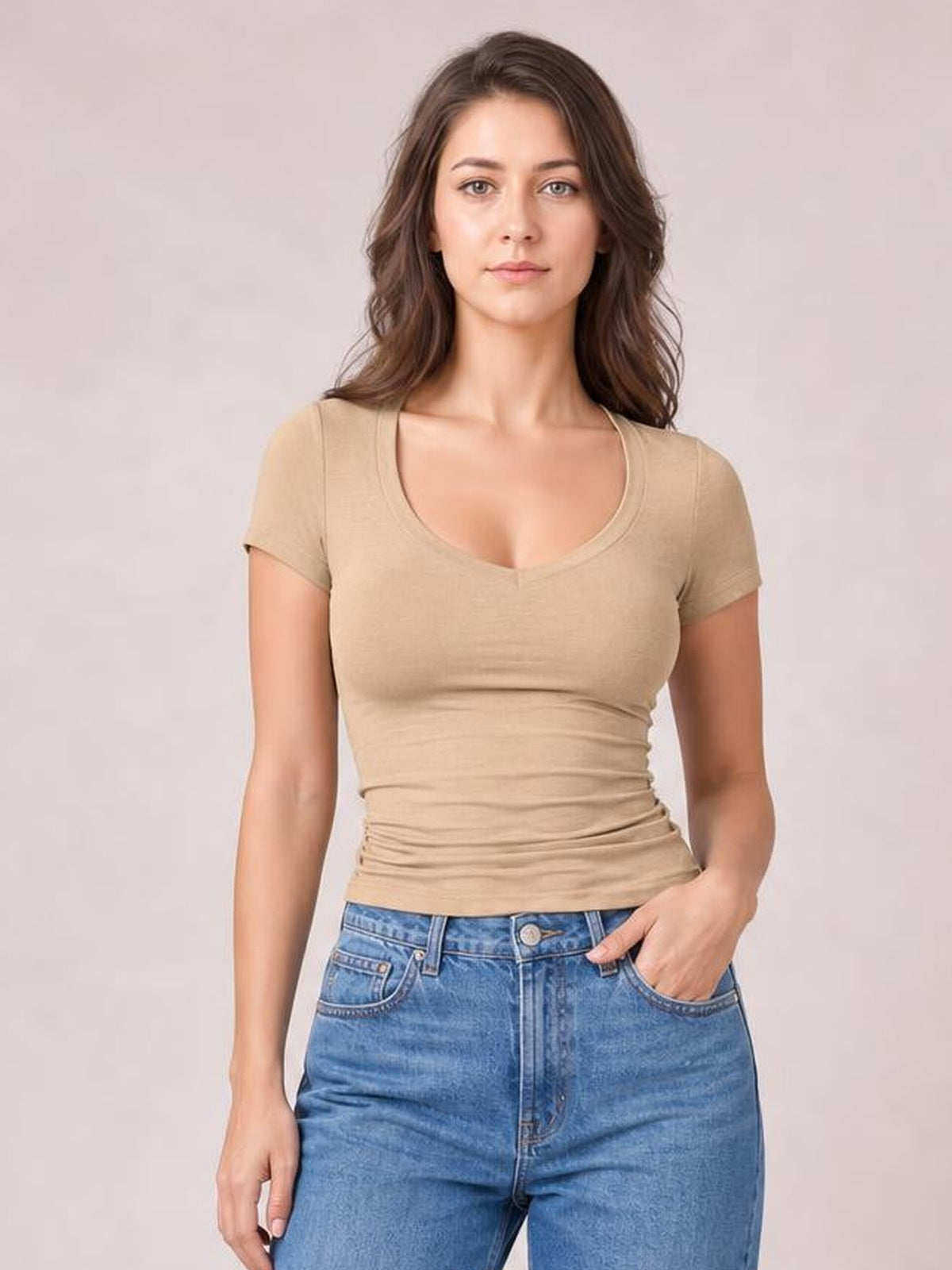 Model wearing a beige scoop neck short sleeve T-shirt with a fitted silhouette, ruched lower hem, and smooth basic construction, posed with one hand in her jeans pocket.