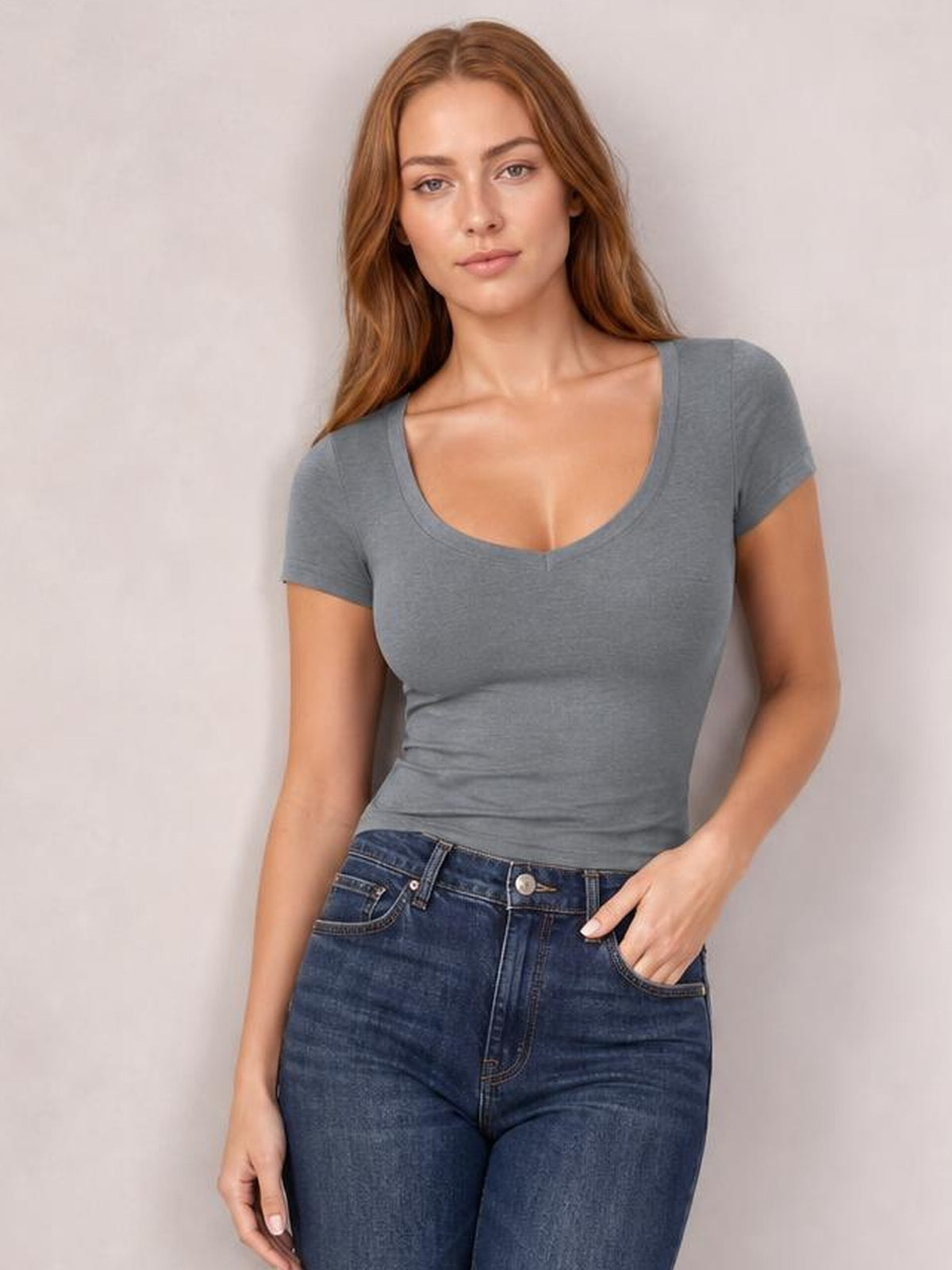 Model wearing a gray scoop neck short sleeve T-shirt with a fitted silhouette and subtle stretch, posed with one hand in her jeans pocket.