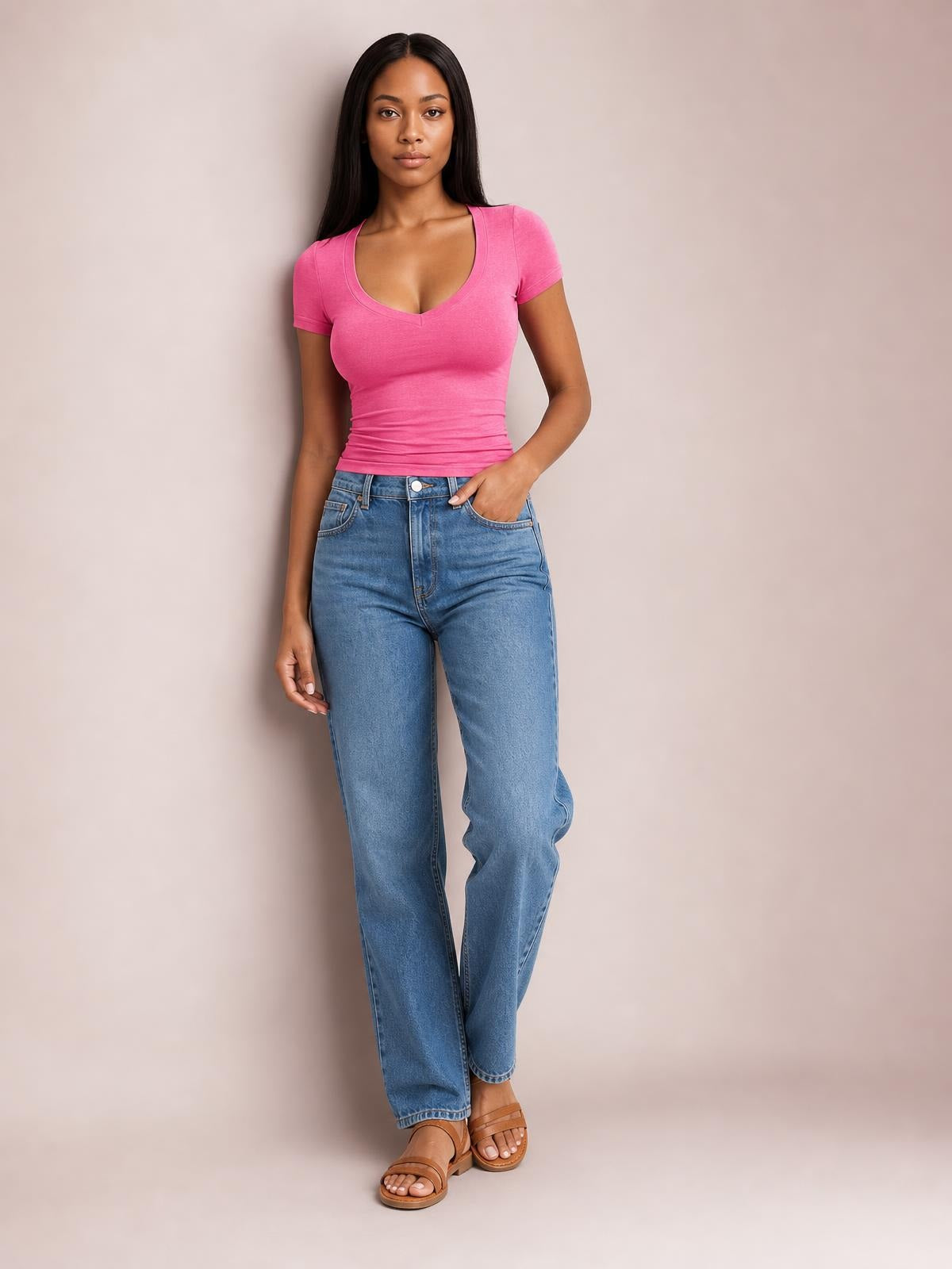 Model wearing a bright pink scoop neck short sleeve T-shirt with a fitted, slightly ruched silhouette, paired with jeans and one hand in a pocket.
