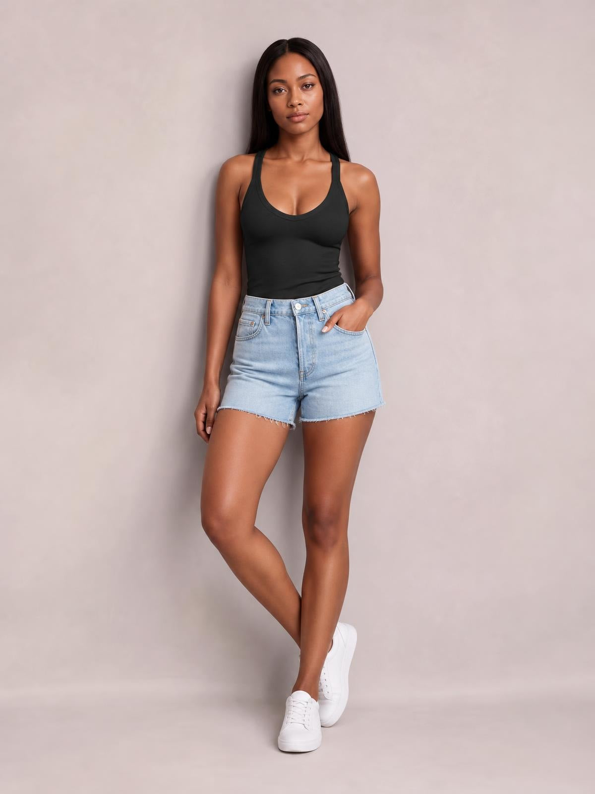 Model poses in a fitted black scoop neck tank with wide straps and a streamlined silhouette, paired with denim shorts and crossed legs.