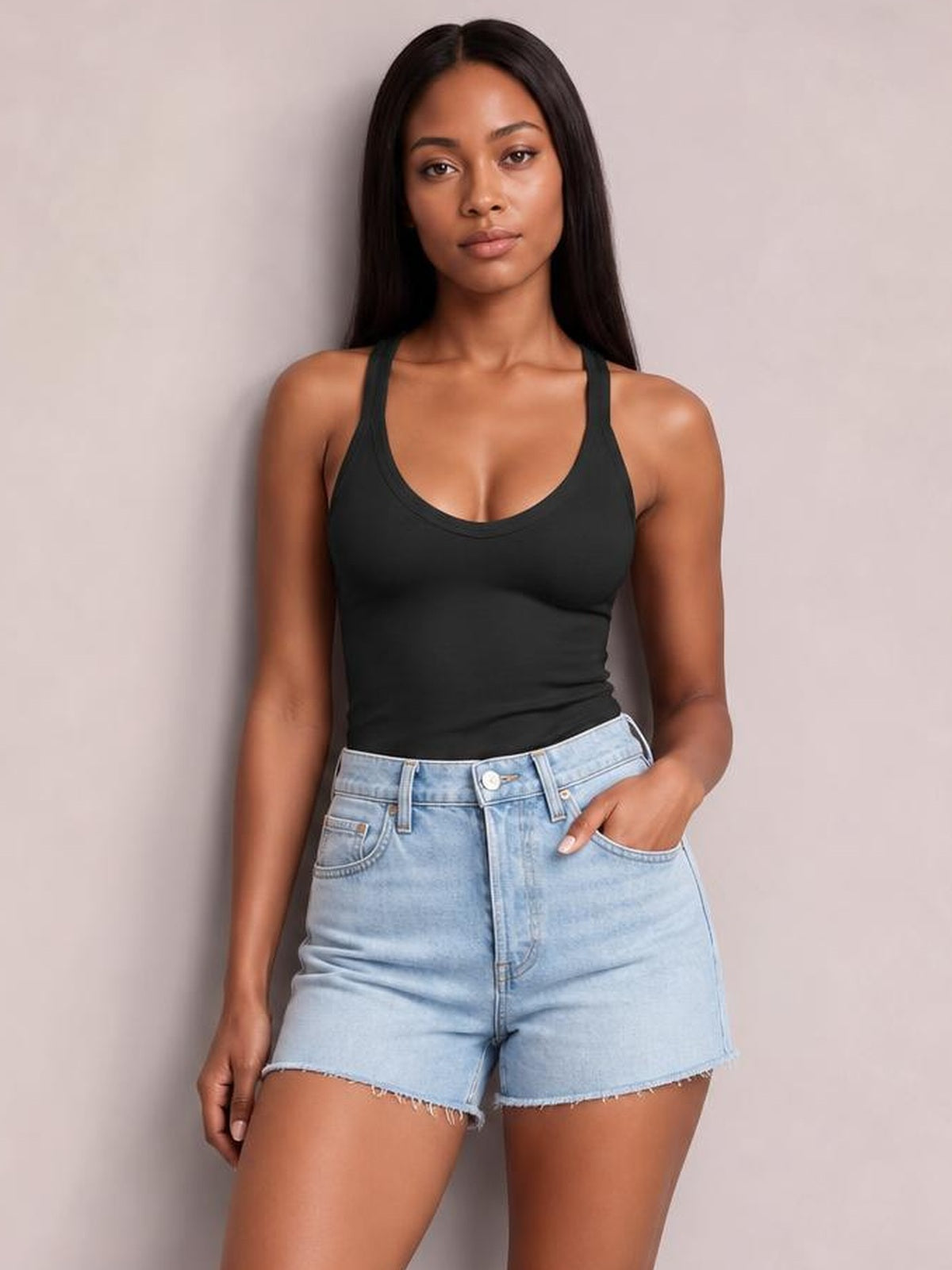 Model wears a black scoop neck wide strap tank with a fitted silhouette and double-stitched neckline, paired with light-wash denim shorts.