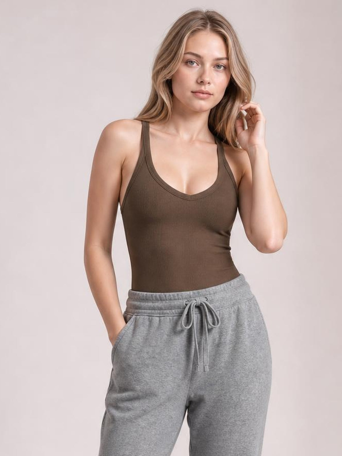 Model wearing a brown scoop neck wide strap tank with a fitted silhouette and subtle ribbed texture, posing with one hand in her pocket.