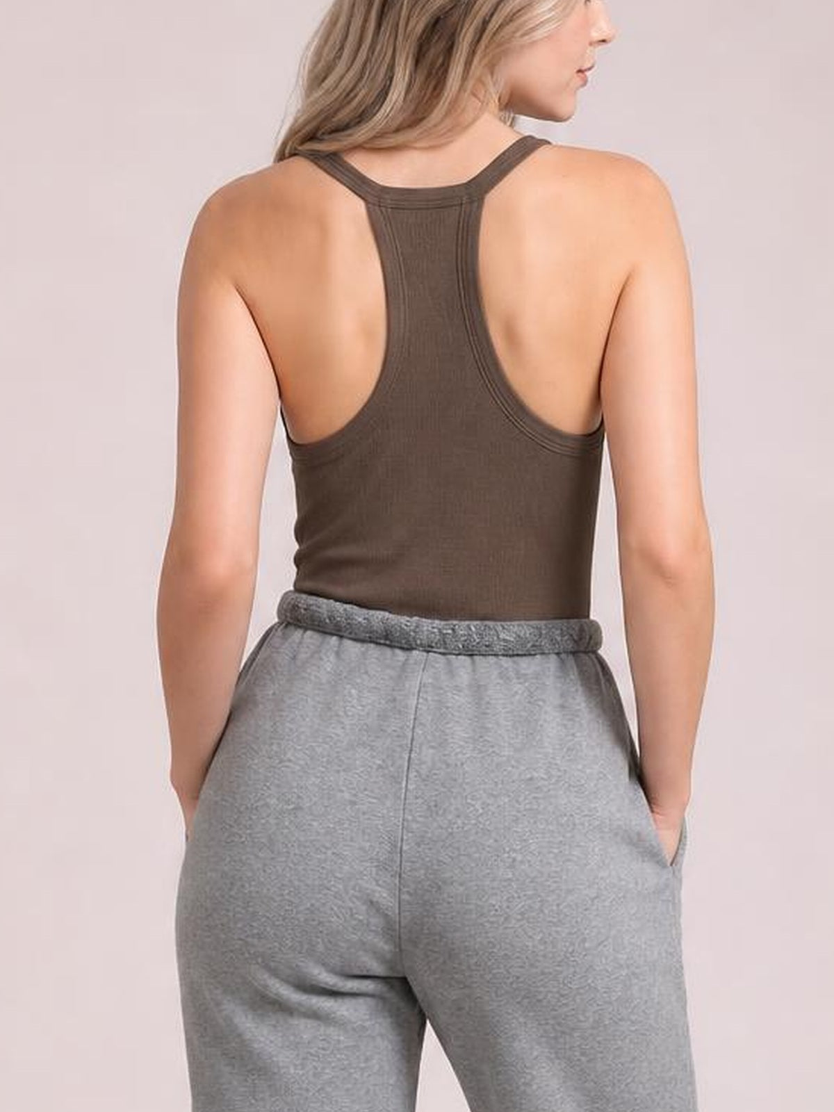 A model stands facing away in a fitted dark brown tank with wide straps, a racerback-style back, and a smooth, close-fitting silhouette.