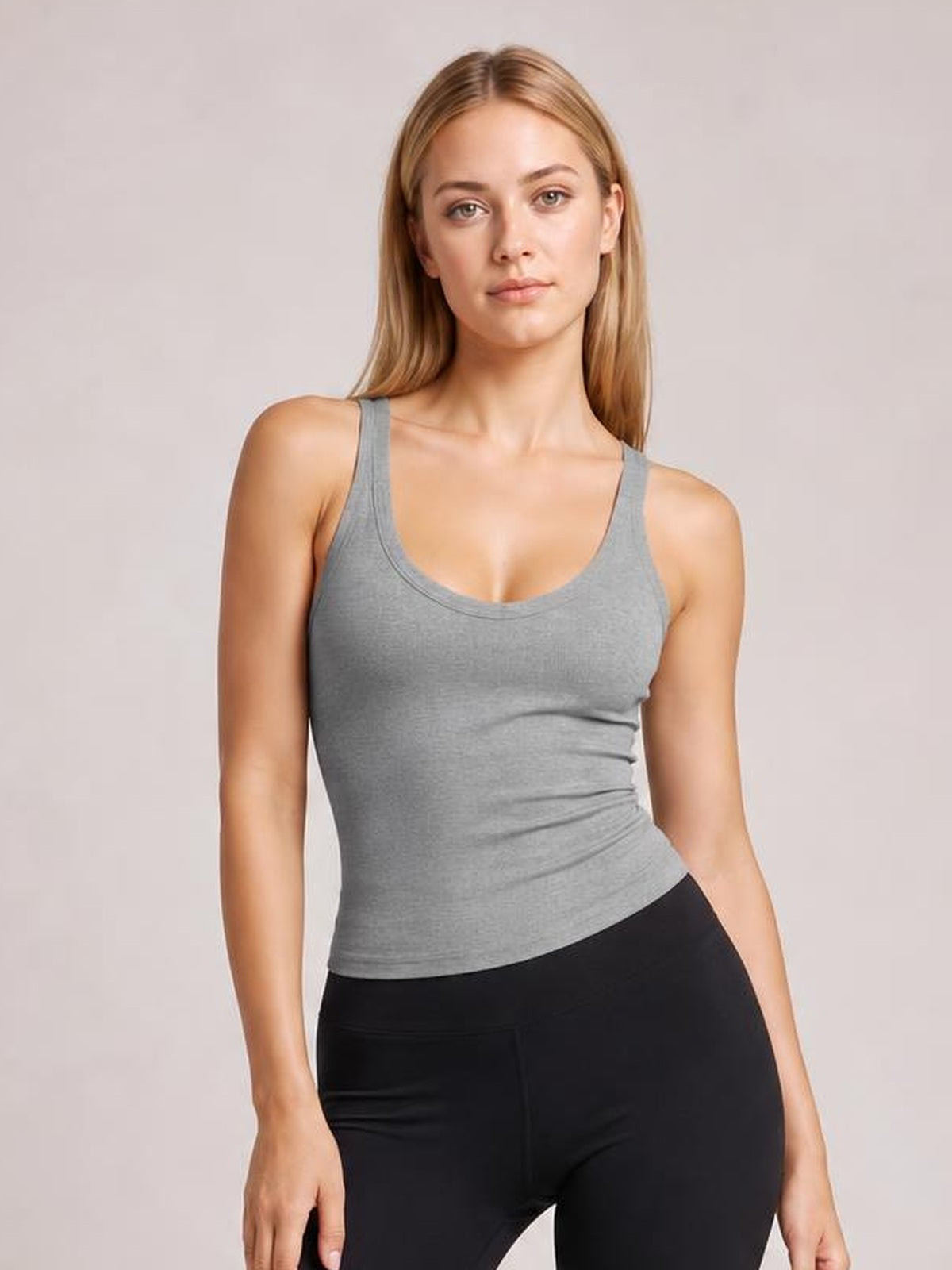 Model wears a fitted gray scoop neck tank with wide straps, a clean bound neckline, and a sleeveless silhouette, posed facing forward.