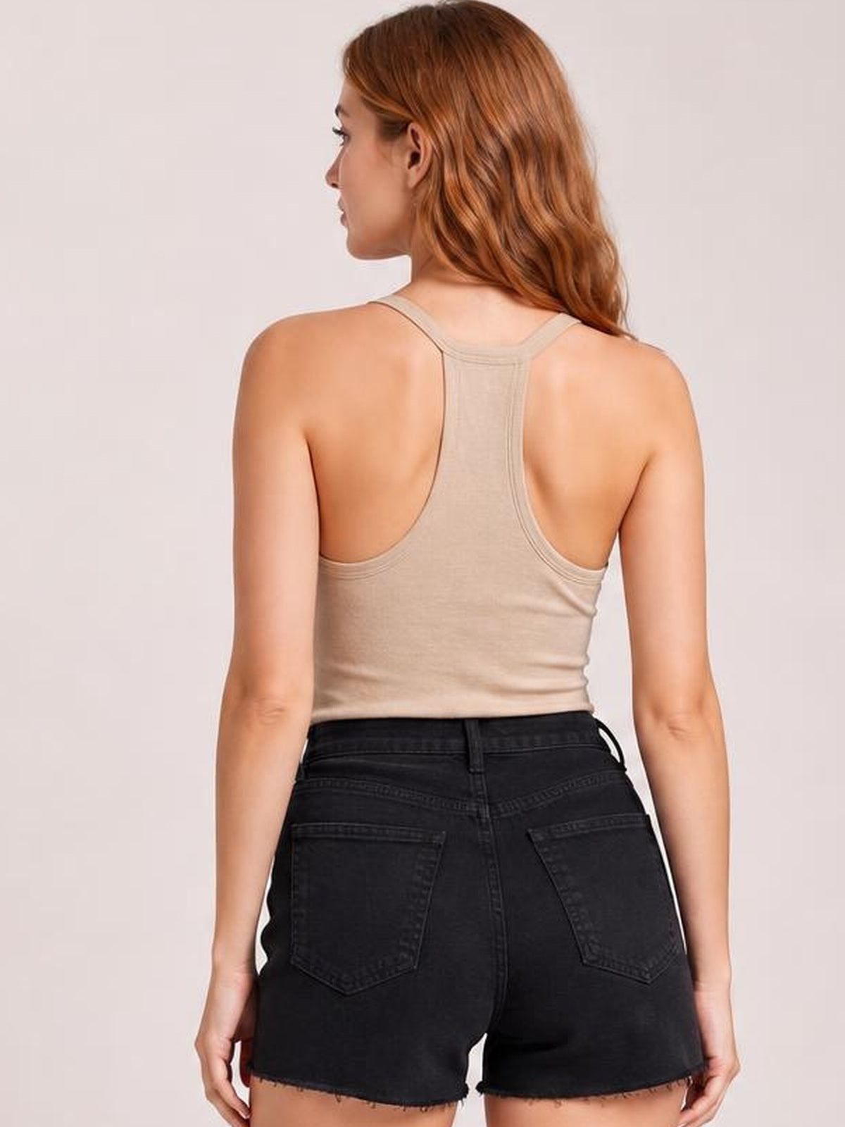 Back view of a model wearing a beige scoop neck wide strap tank with a fitted silhouette, racerback construction, and moderate stretch.