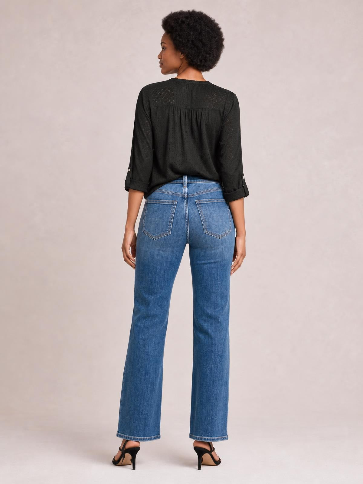 A model stands facing away in medium-wash blue seam detail jeans with a straight-leg silhouette, belt loops, and two back patch pockets.
