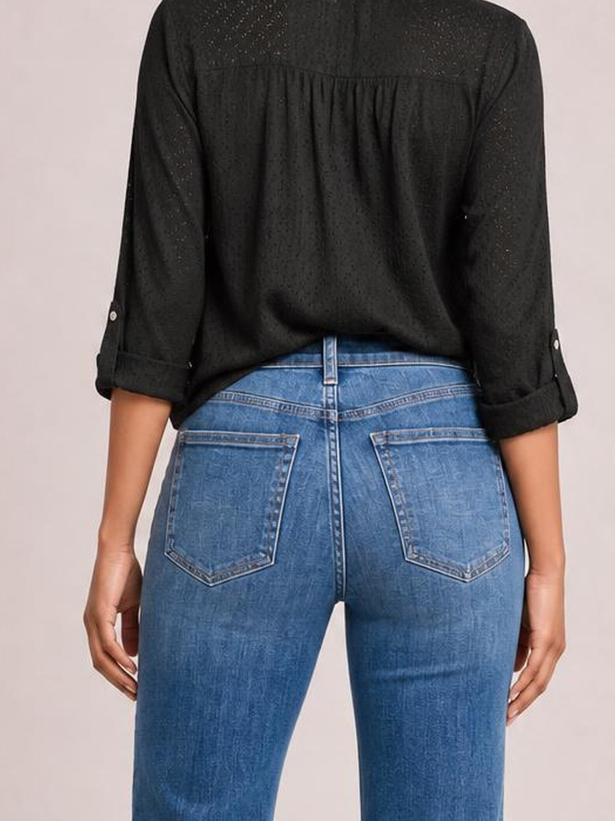 A standing model wears blue seam-detail jeans shown from the back, featuring belt loops, contrast stitching, and two large patch back pockets.