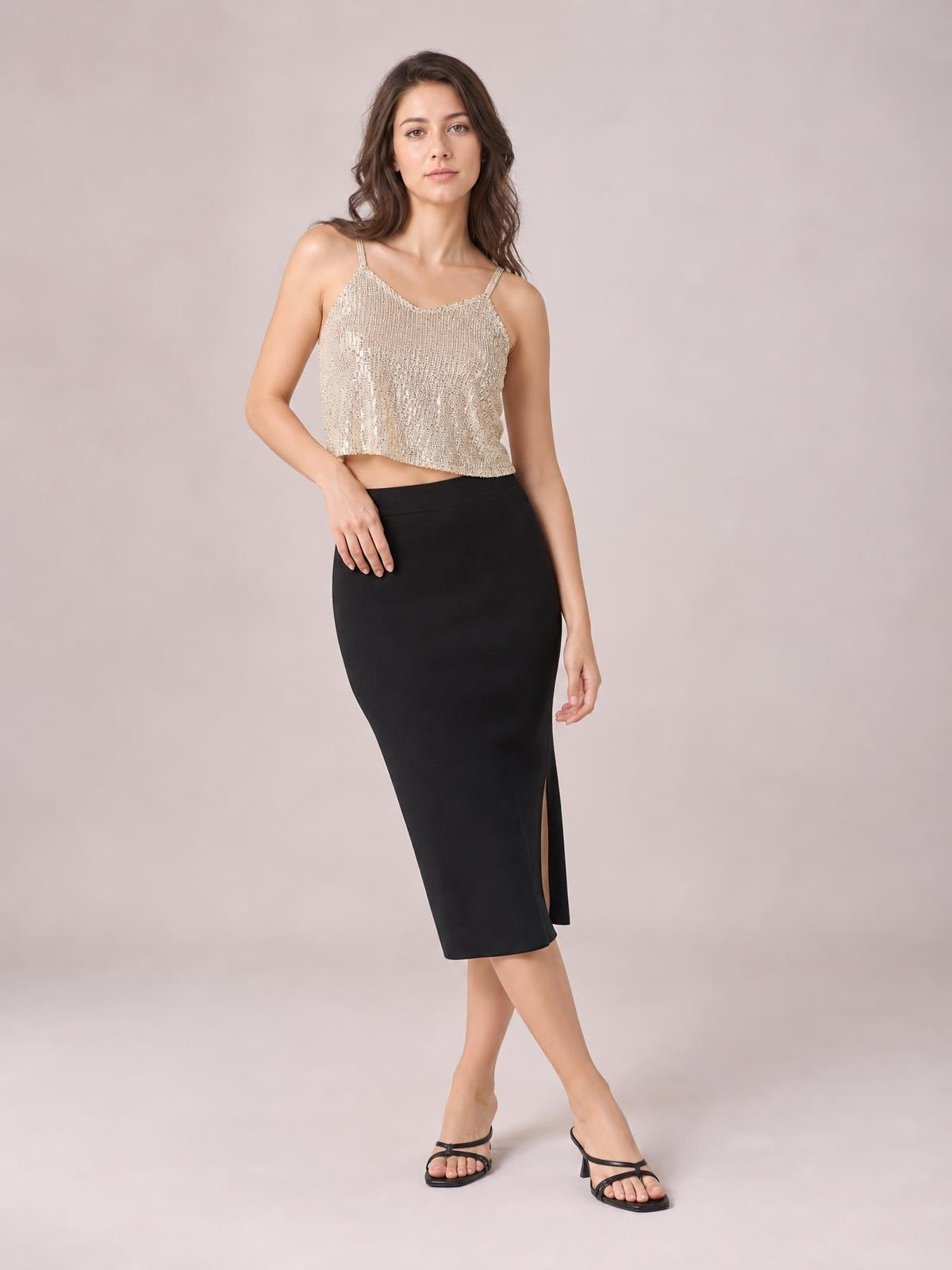 Model poses in a champagne sequin cropped cami with spaghetti straps, a scoop neckline, sleeveless cut, and a relaxed straight silhouette.