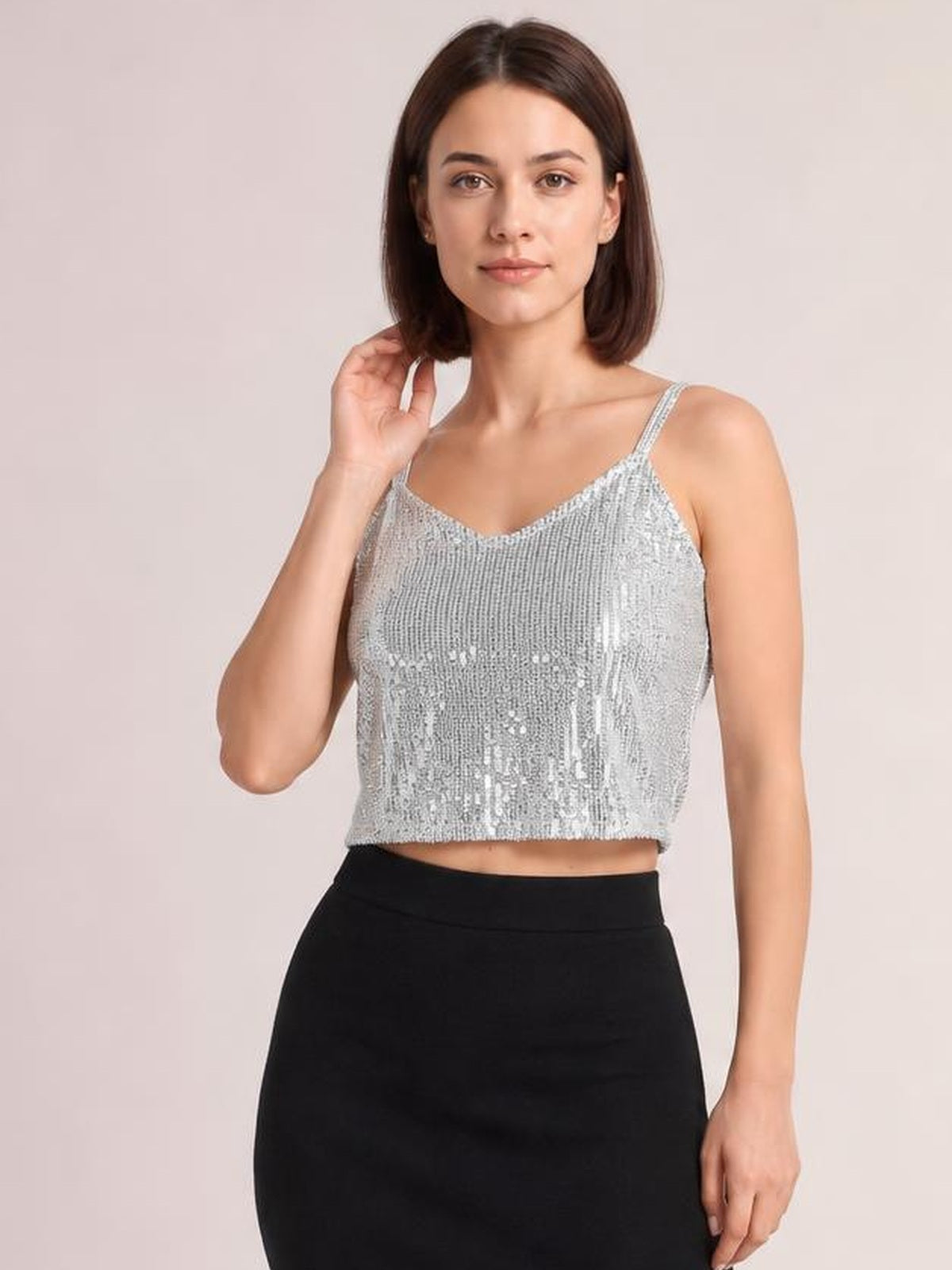 Model poses with one hand near her hair, wearing a silver sequin cropped cami with a V-neck, spaghetti straps, and a fitted silhouette.