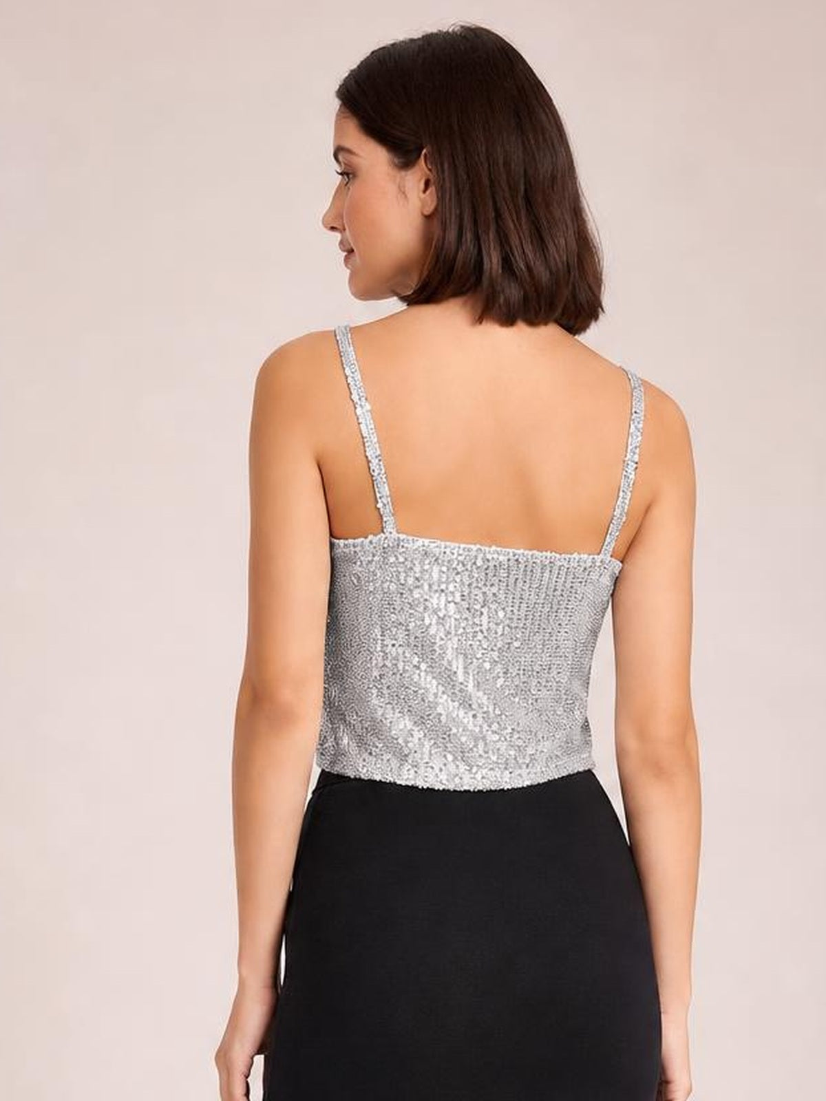 A model turns to show a silver sequin cropped cami with slim spaghetti straps, a straight back neckline, and a fitted silhouette.