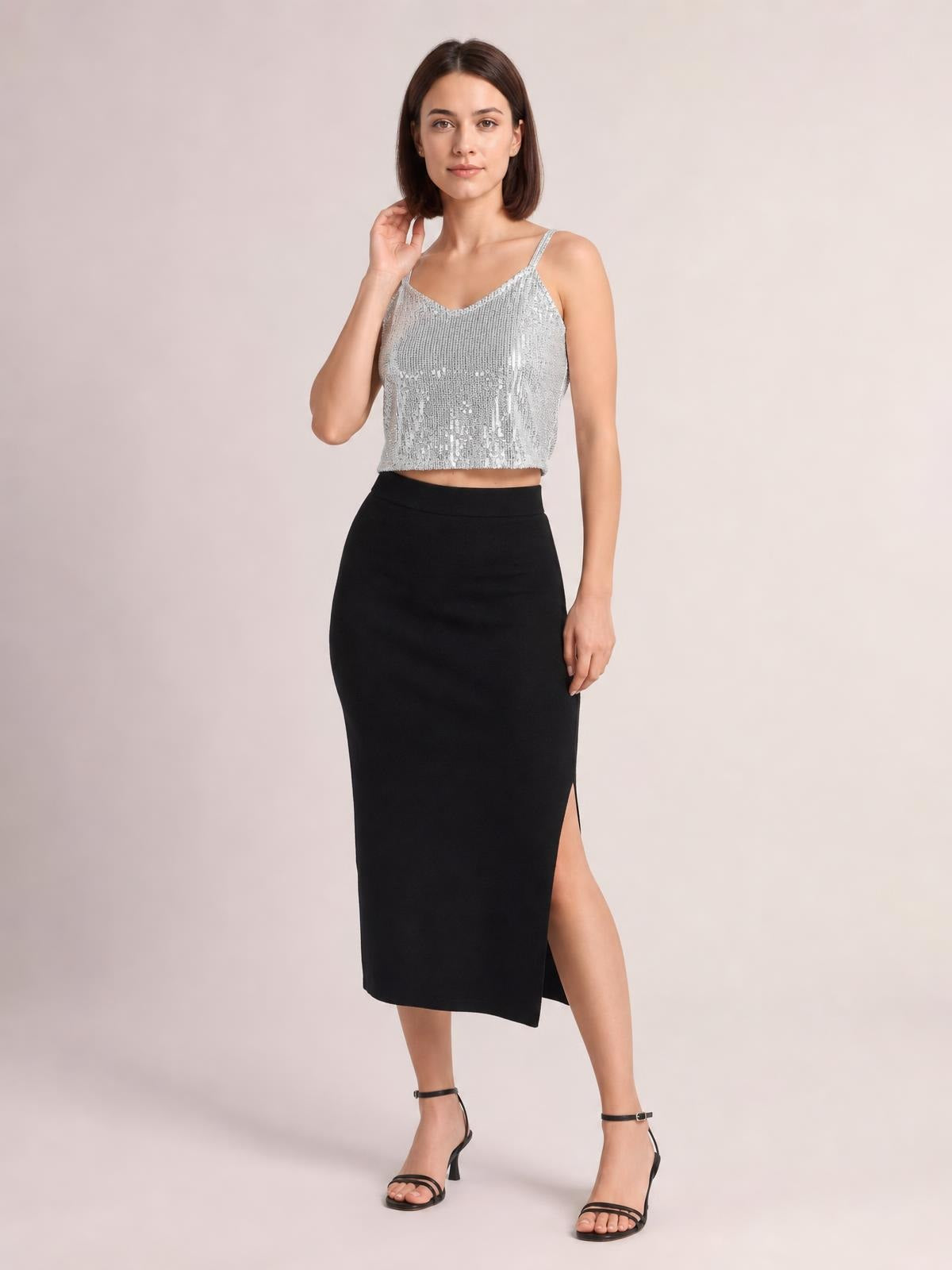 Model poses in a silver sequin cropped cami with a V-neck, slender spaghetti straps, and a fitted sleeveless silhouette.