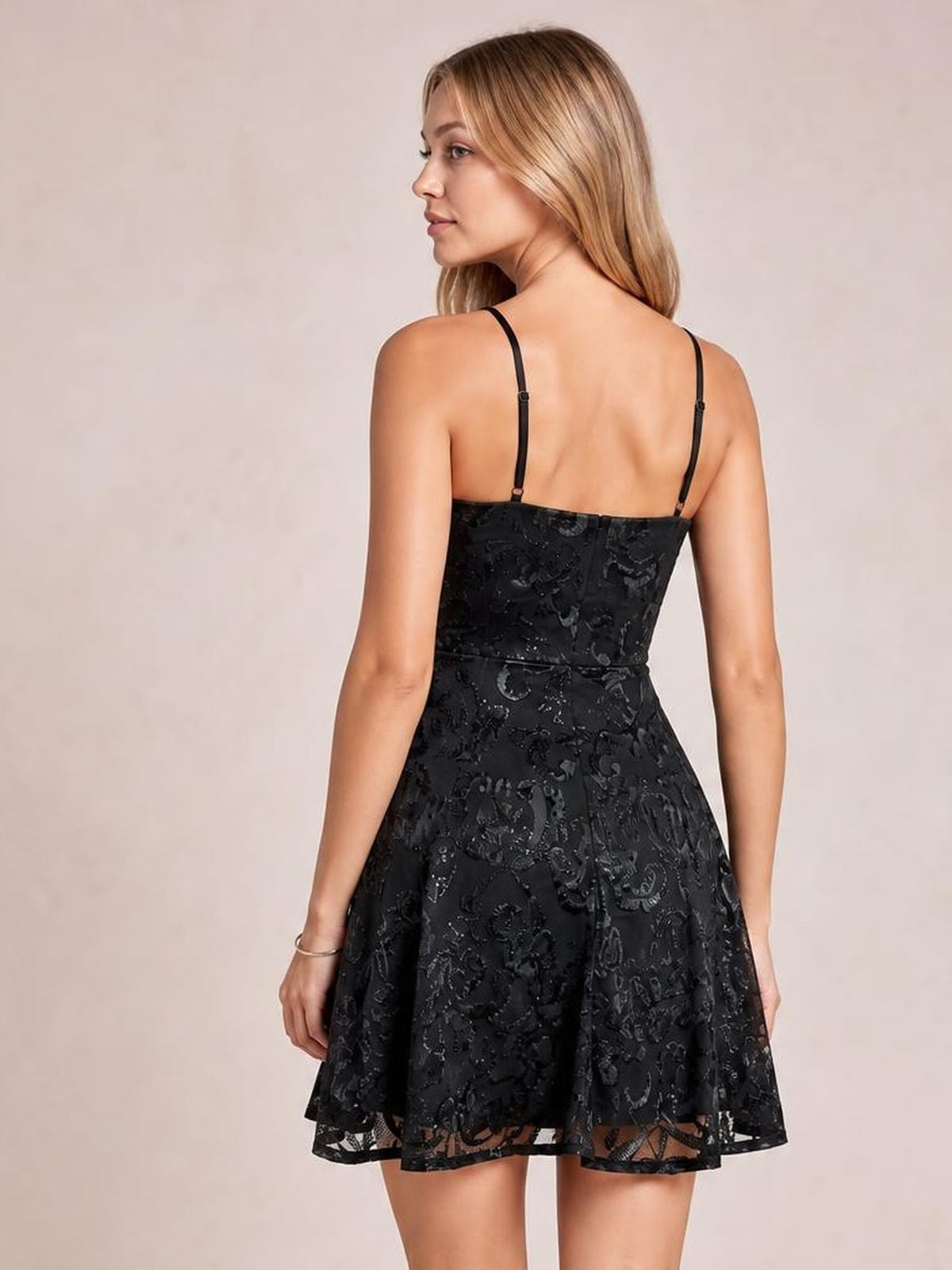 A model stands in a back-facing pose wearing a black sequin-embellished mini dress with slender straps, a fitted mid waist, and a flared skirt.