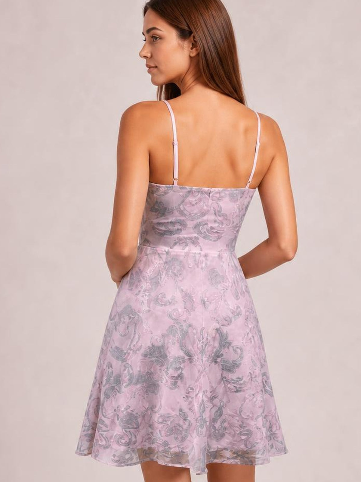 A model poses from the back in a pink sequin-embellished mini dress with thin straps, a fitted mid-waist bodice, and flared skirt silhouette.