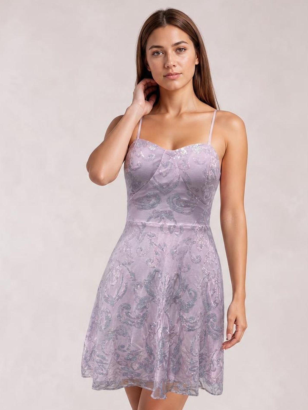 A model poses in a lavender sequin-embellished mini dress with thin straps, a fitted bodice, defined mid waist, and flared paisley-patterned skirt.