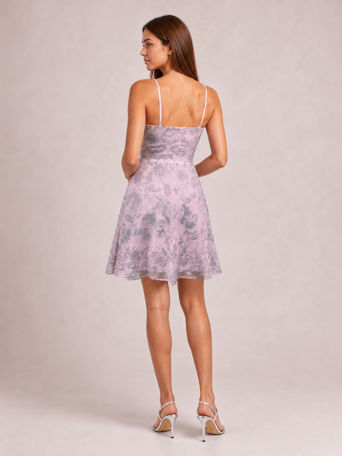 A model stands facing away in a pink sequin embellished mini dress with slim adjustable straps, a mid waist, fitted bodice, and flared skirt.