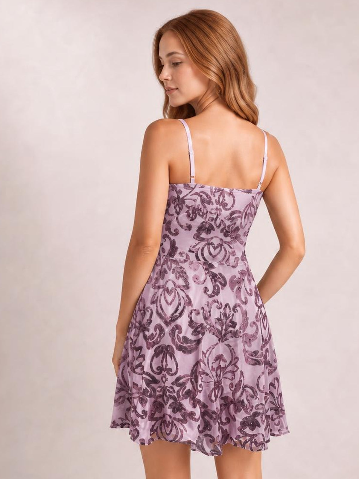 A model poses from the back in a lavender sequin-embellished mini dress with thin straps, a fitted mid-waist bodice, and a flared skirt.