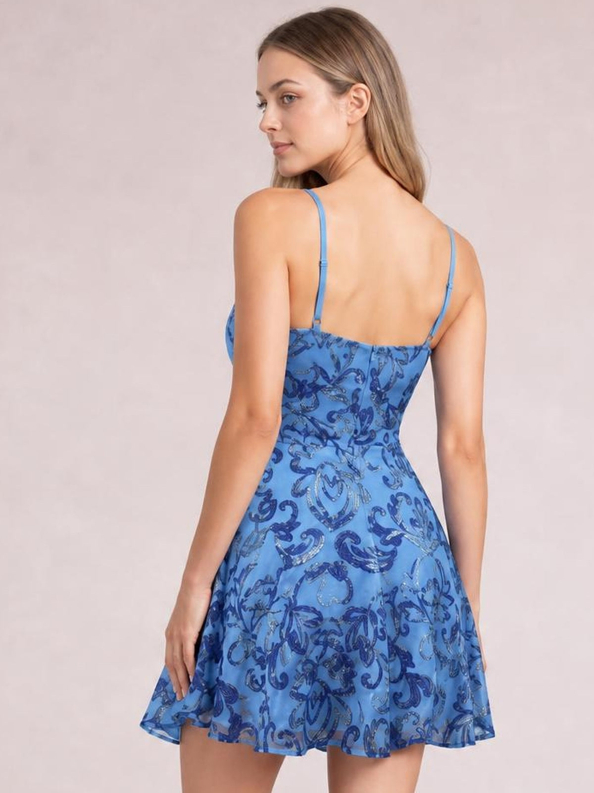 A model wears a blue sequin-embellished mini dress with thin adjustable straps, a fitted mid-waist bodice, and a flared skirt, shown from the back.