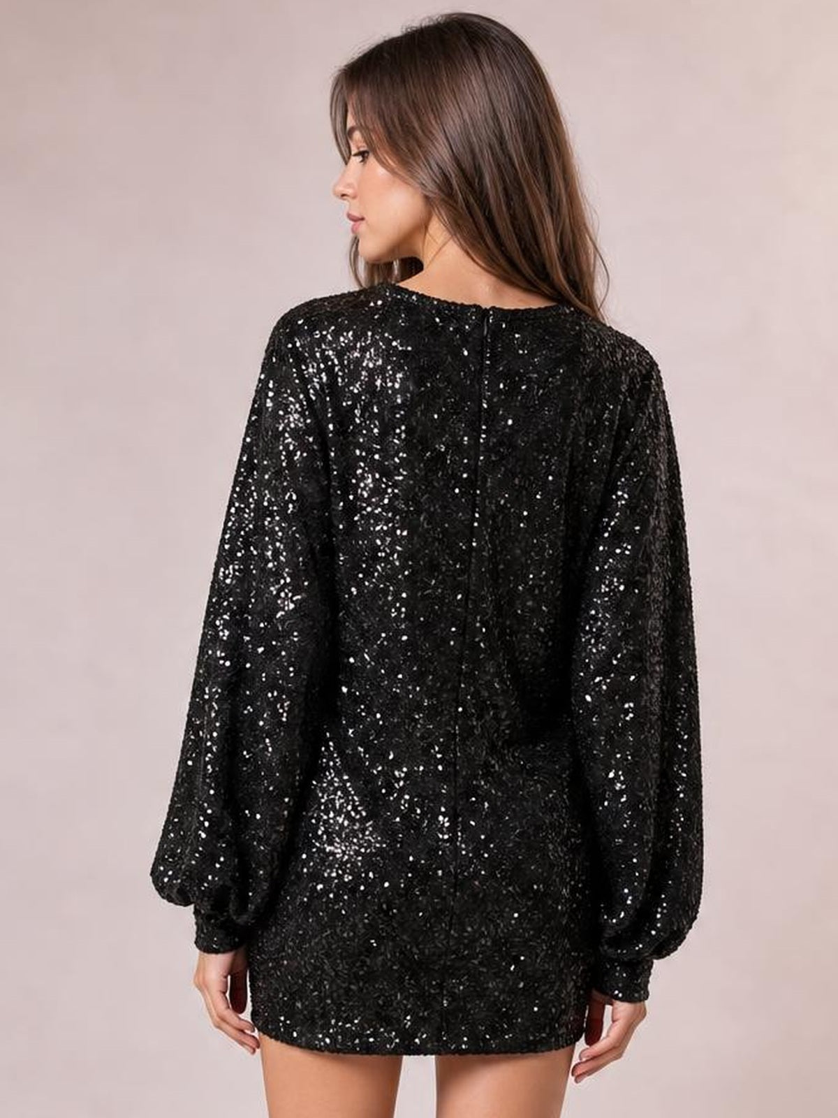 Model shown from the back in a black sequined long-sleeve mini dress with a relaxed silhouette, center-back zipper, and softly gathered sleeve cuffs.